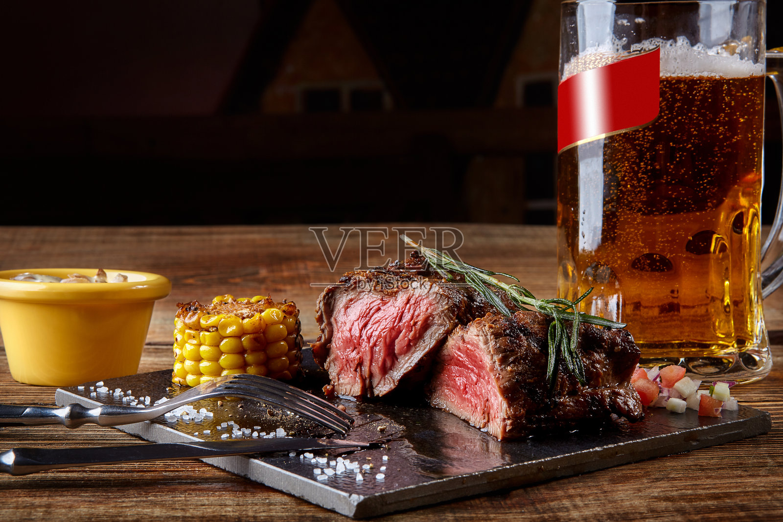烤里脊牛排，烤牛肉和蘑菇酱在黑色砧板上和一杯啤酒在木桌上照片摄影图片