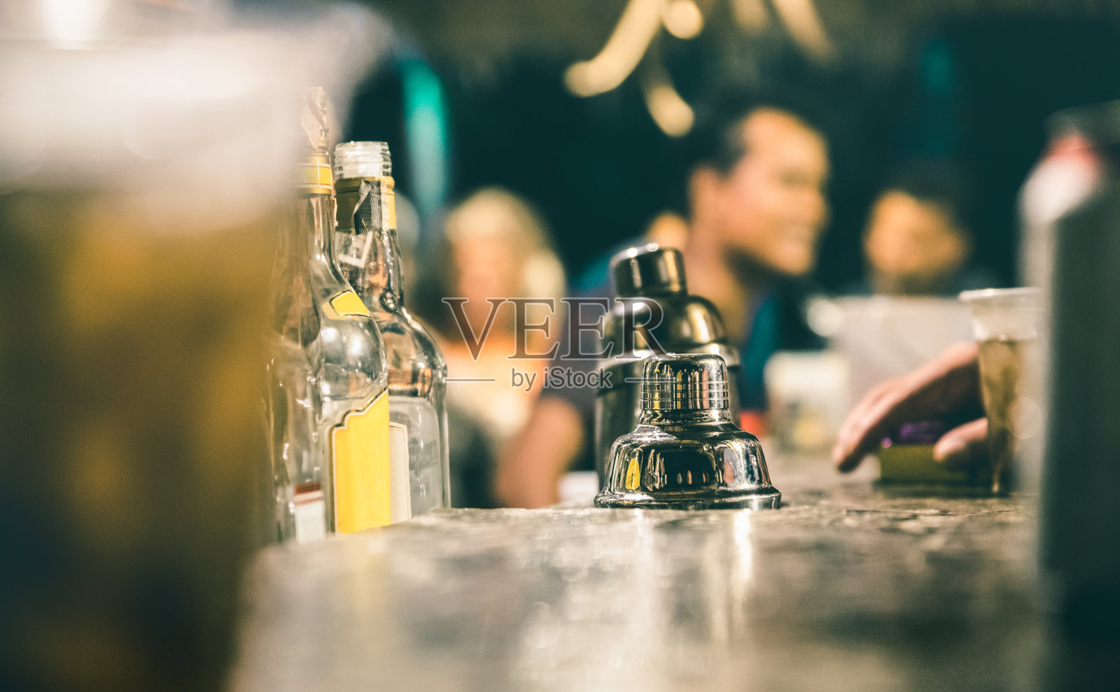 模糊的散焦侧面的酒保和人们喝酒和在鸡尾酒吧的乐趣-社会聚会概念与人们享受时间在一起-复古的蓝绿色滤镜与焦点在摇壶照片摄影图片