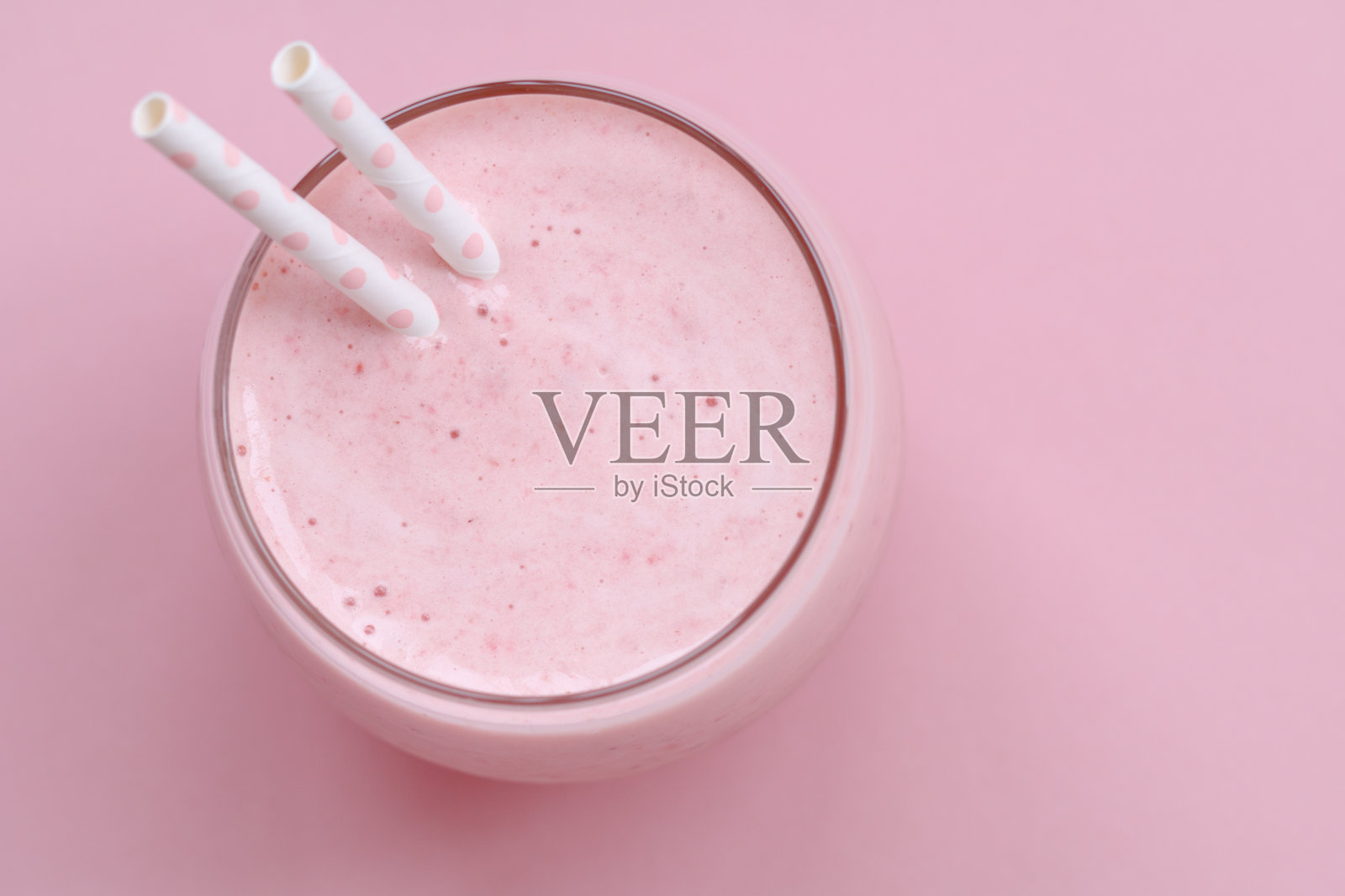 粉色草莓冰沙，用一根吸管在粉红色的背景上。夏日健康生活理念。照片摄影图片