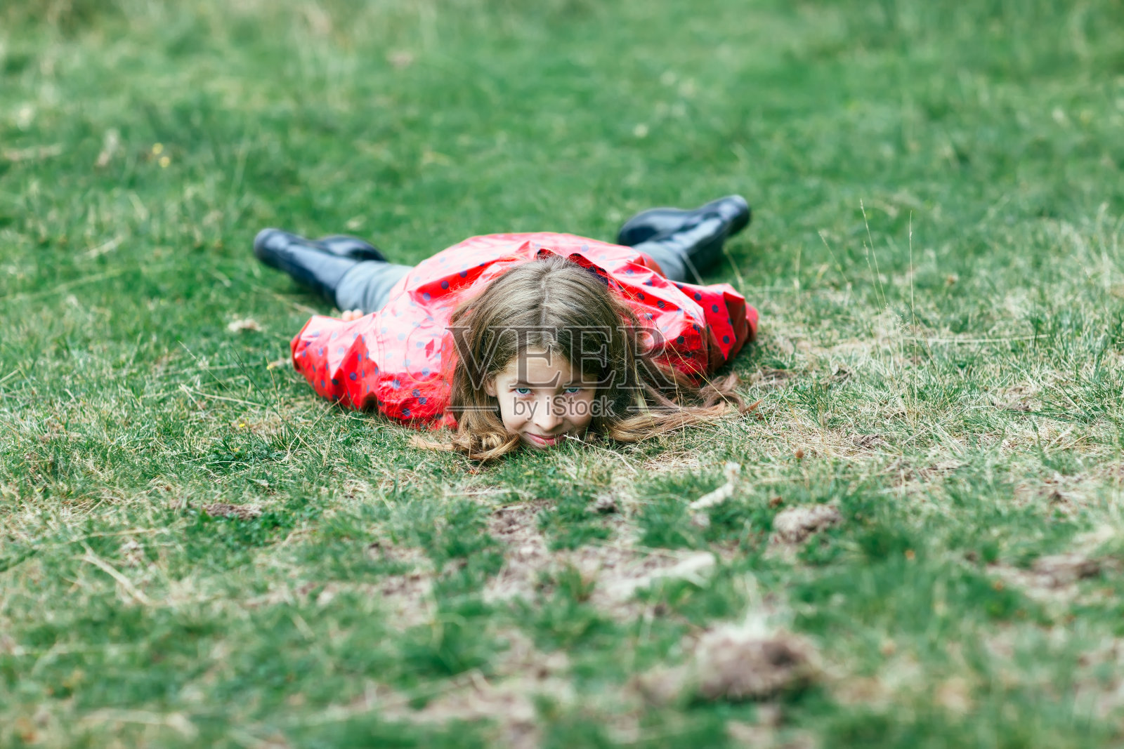 穿着粉红色夹克的小女孩躺在草地上，看着镜头照片摄影图片