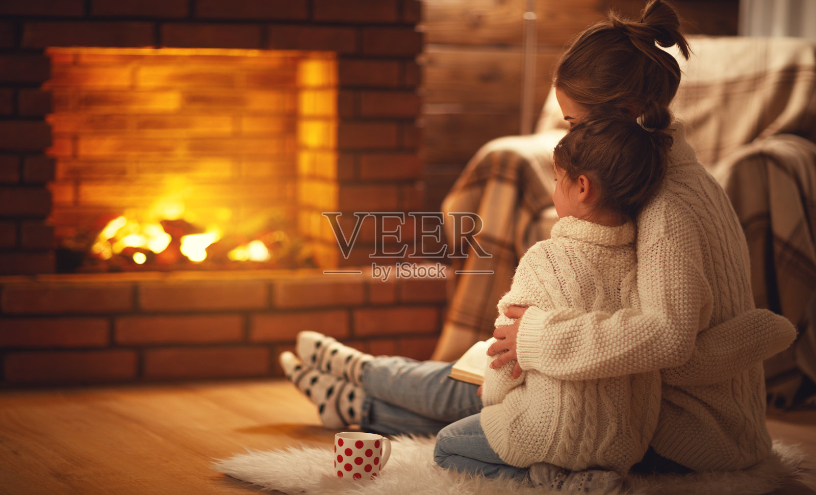 在冬天的夜晚，家庭母亲和孩子拥抱在壁炉旁取暖照片摄影图片