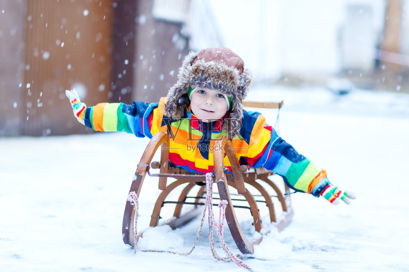 一个小男孩喜欢在下雪的时候坐雪橇。快乐的学龄前儿童坐在老式雪橇上。照片摄影图片