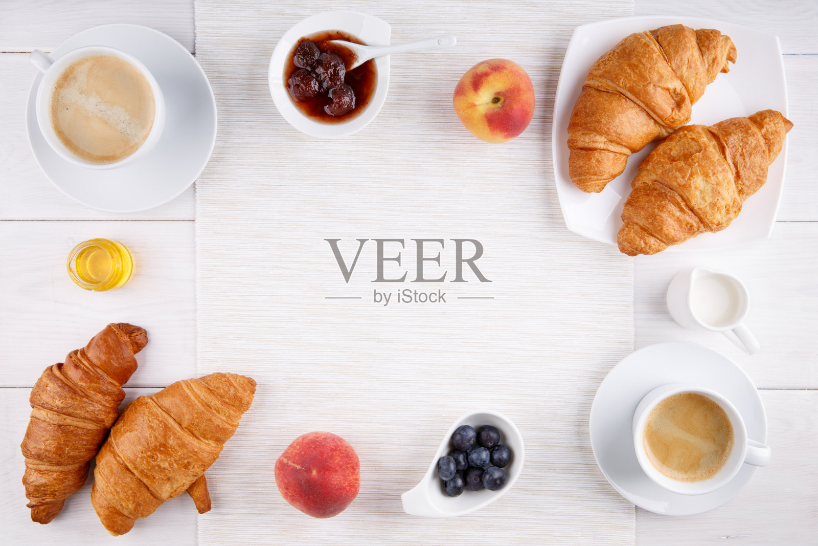 早餐:两杯咖啡，牛角面包，果酱，蜂蜜和水果放在白色的桌子上。前视图。副本的空间。照片摄影图片