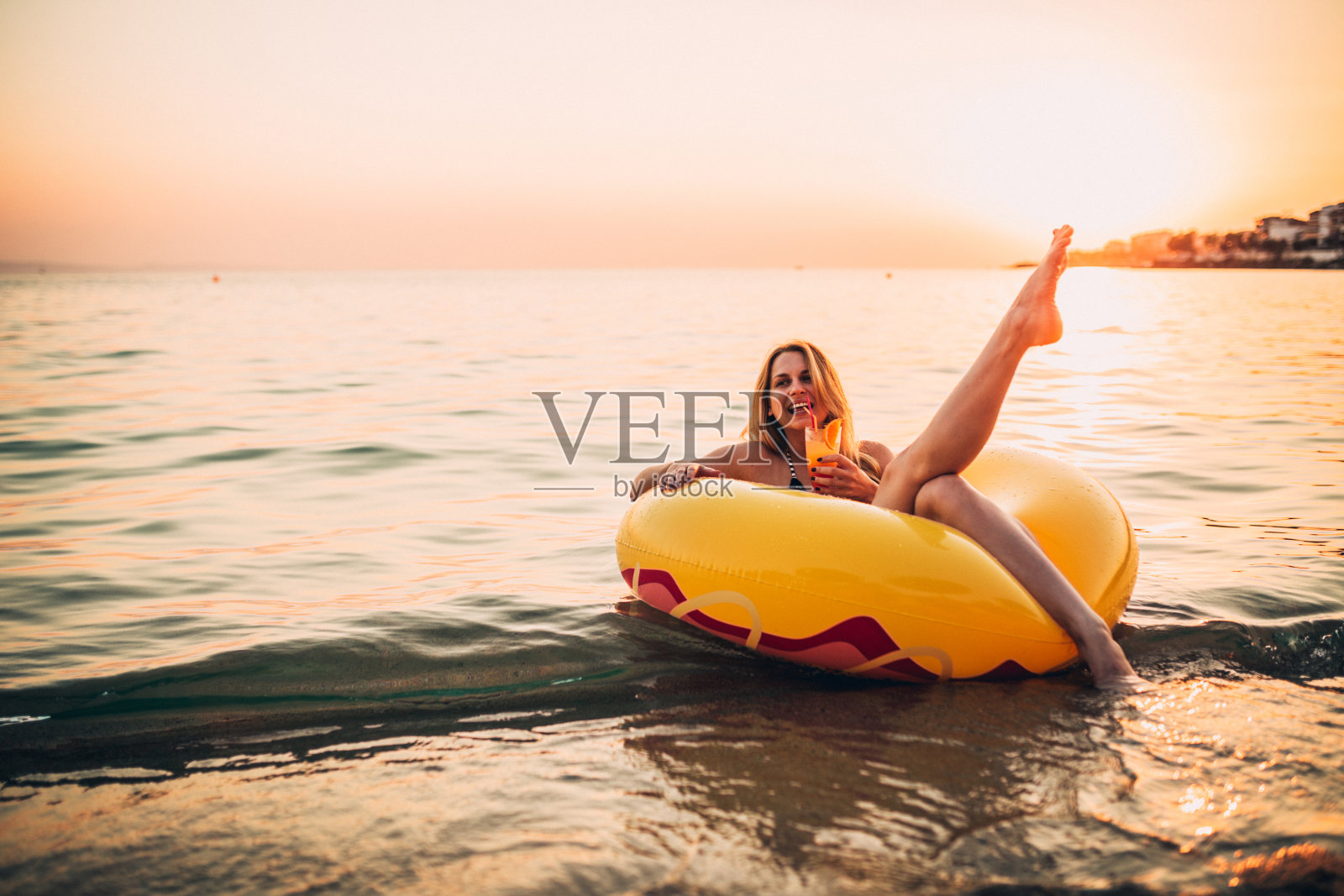 年轻女子浮在水面，喝着鸡尾酒龙舌兰，在一个美丽的夏日日出照片摄影图片