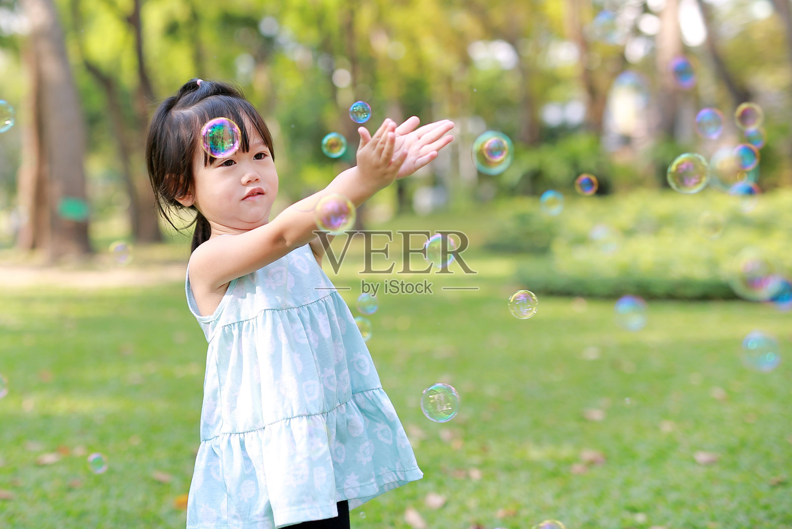 可爱的小女孩在花园里玩泡泡。照片摄影图片