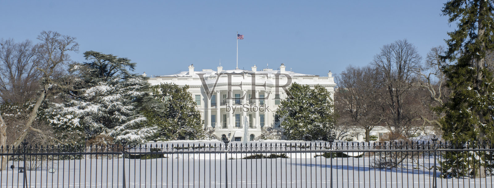 在明亮的蓝天下，白宫和庭院被白雪覆盖。照片摄影图片