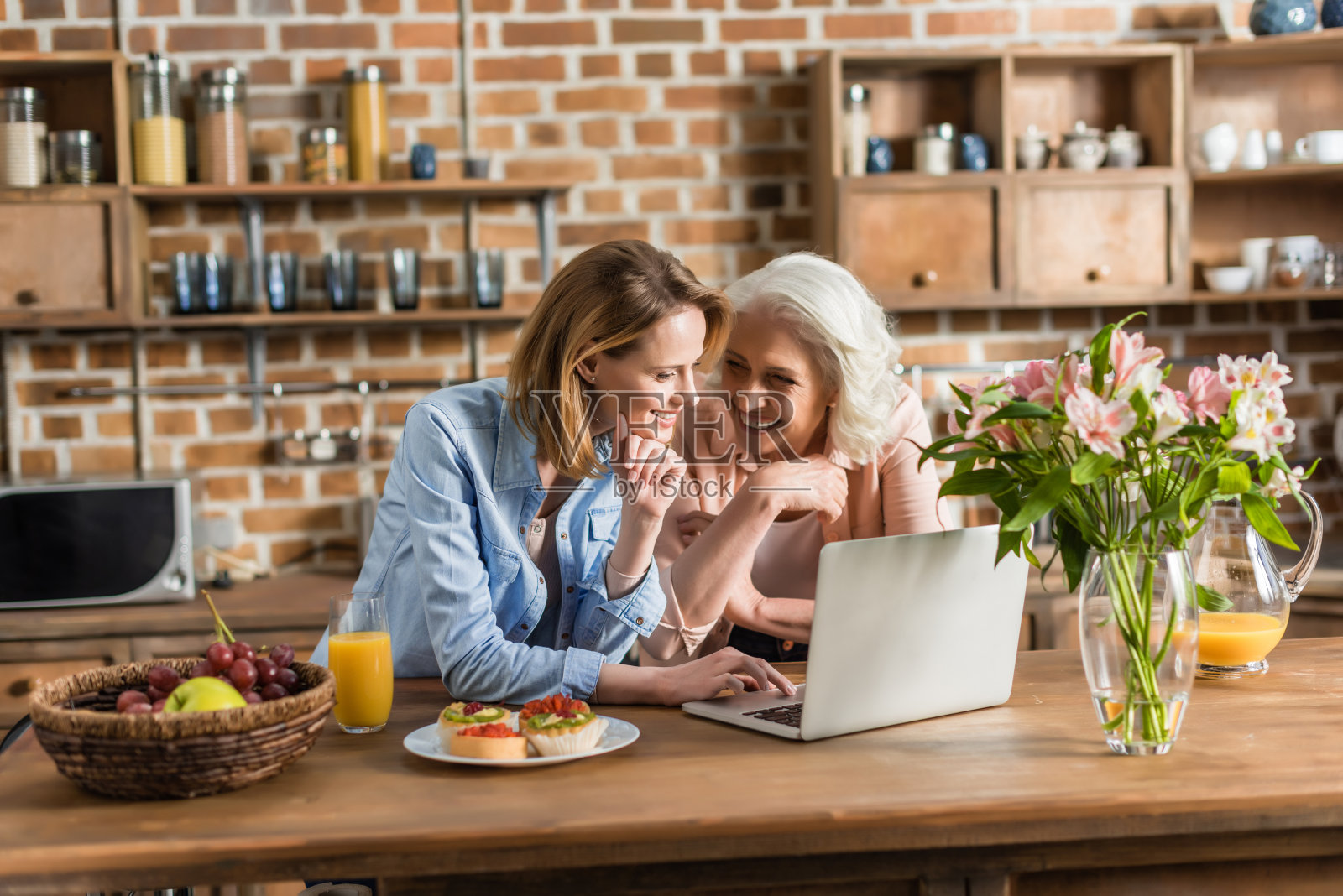 两个女人，老的和年轻的在厨房的桌子上使用笔记本电脑照片摄影图片