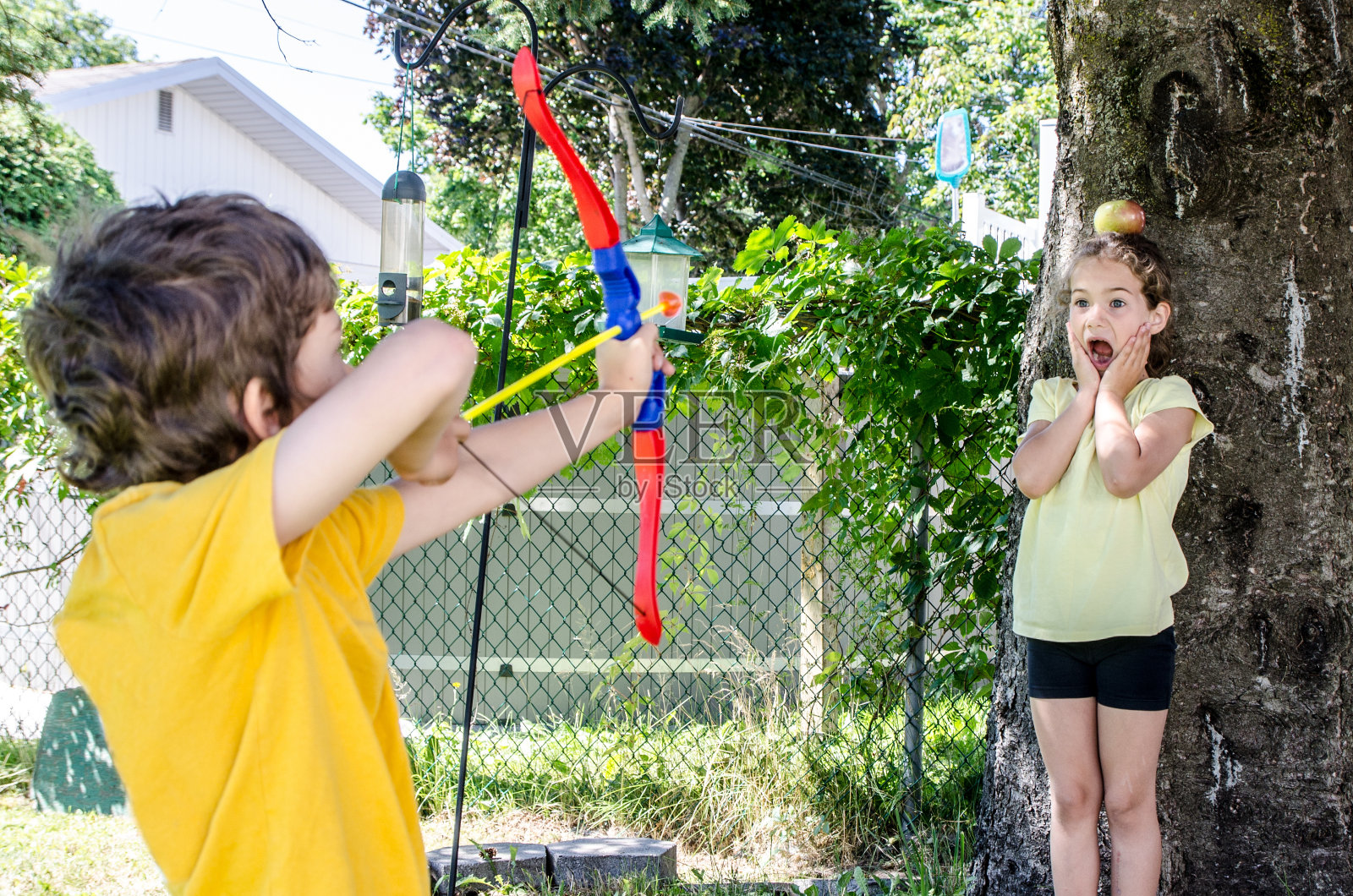 夏日里，一个小男孩拿着弓箭瞄准他妹妹头上的苹果照片摄影图片