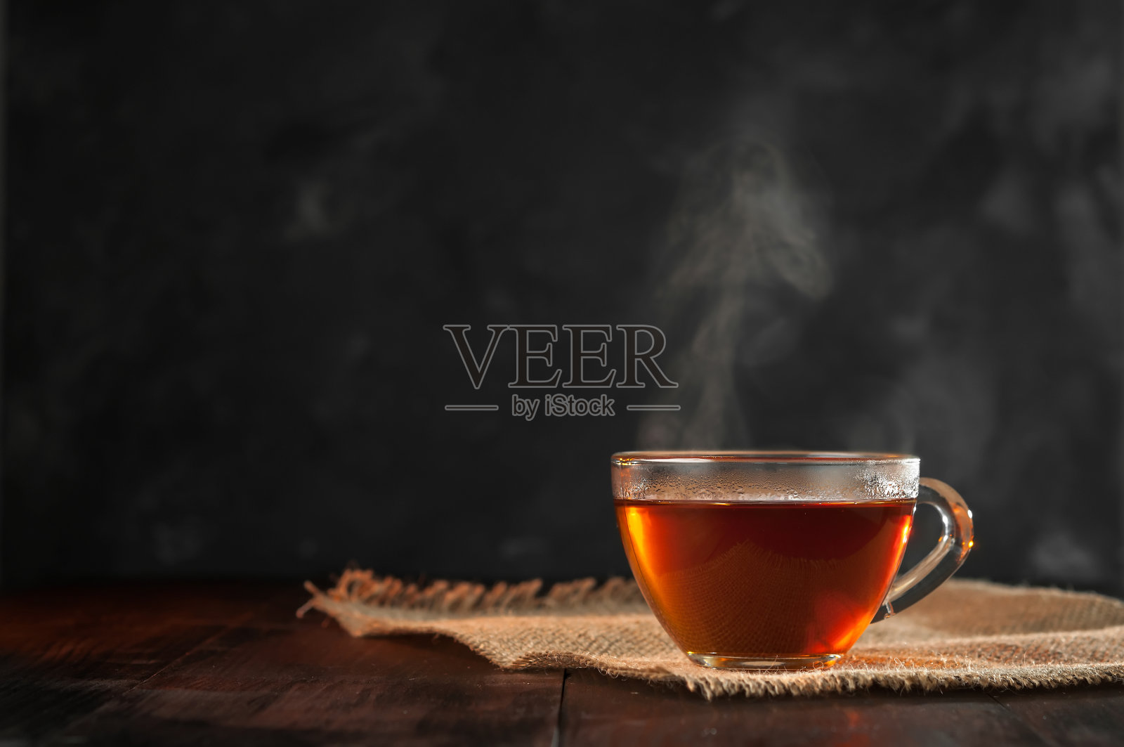 一杯新泡的红茶，逸出蒸汽，温暖柔和的光线，较暗的背景。照片摄影图片