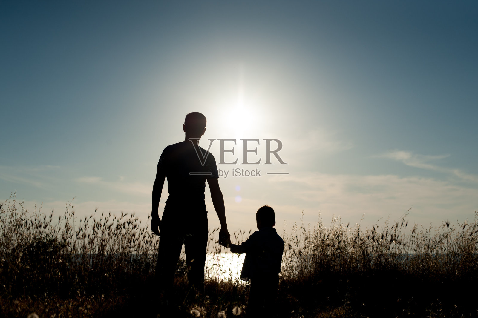 一个成年男子和一个小男孩的剪影映衬着海面上的夕阳照片摄影图片