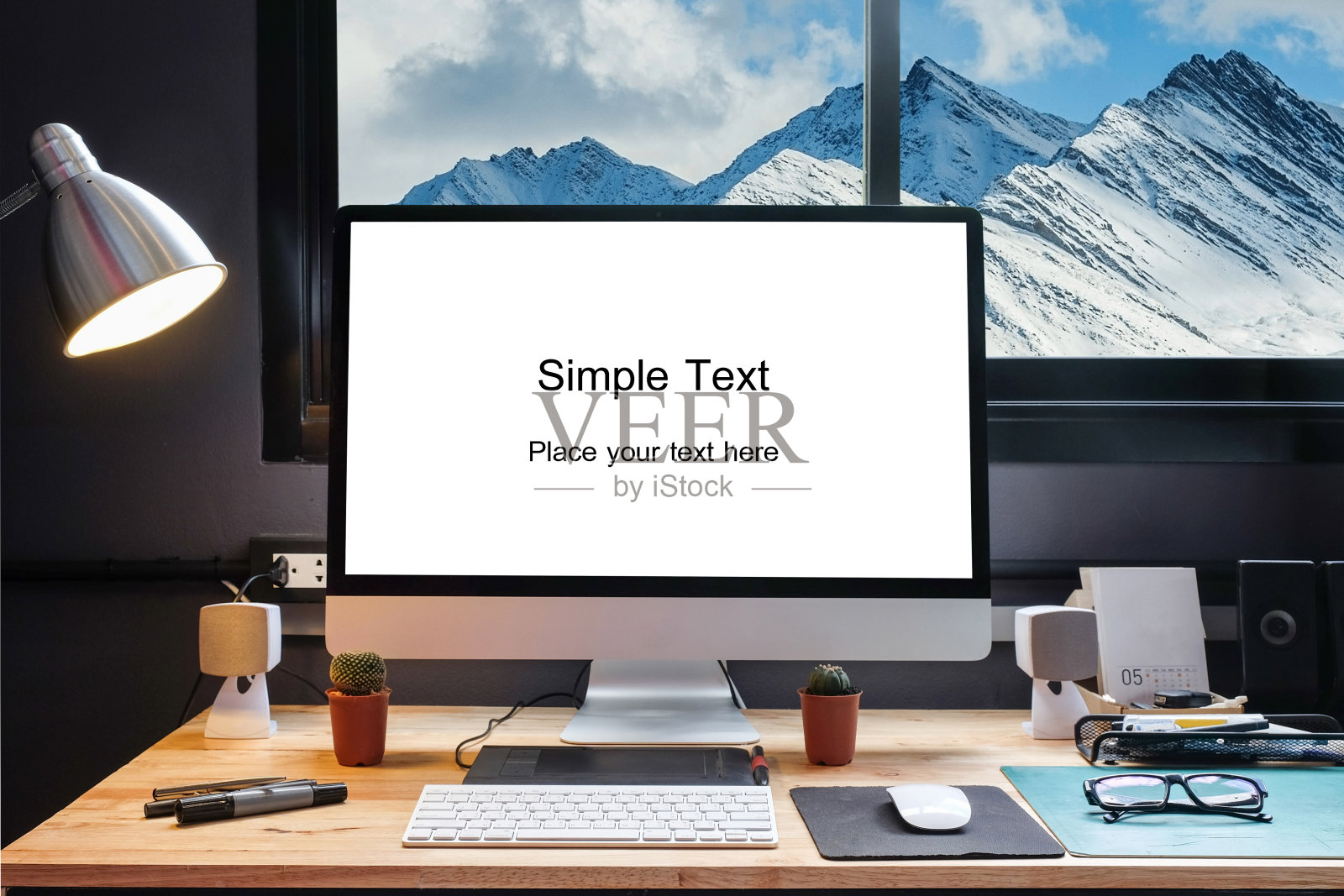平面设计师的工作空间配备了一个笔板，一台电脑和白色的文本屏幕与美丽的雪山从窗口照片摄影图片