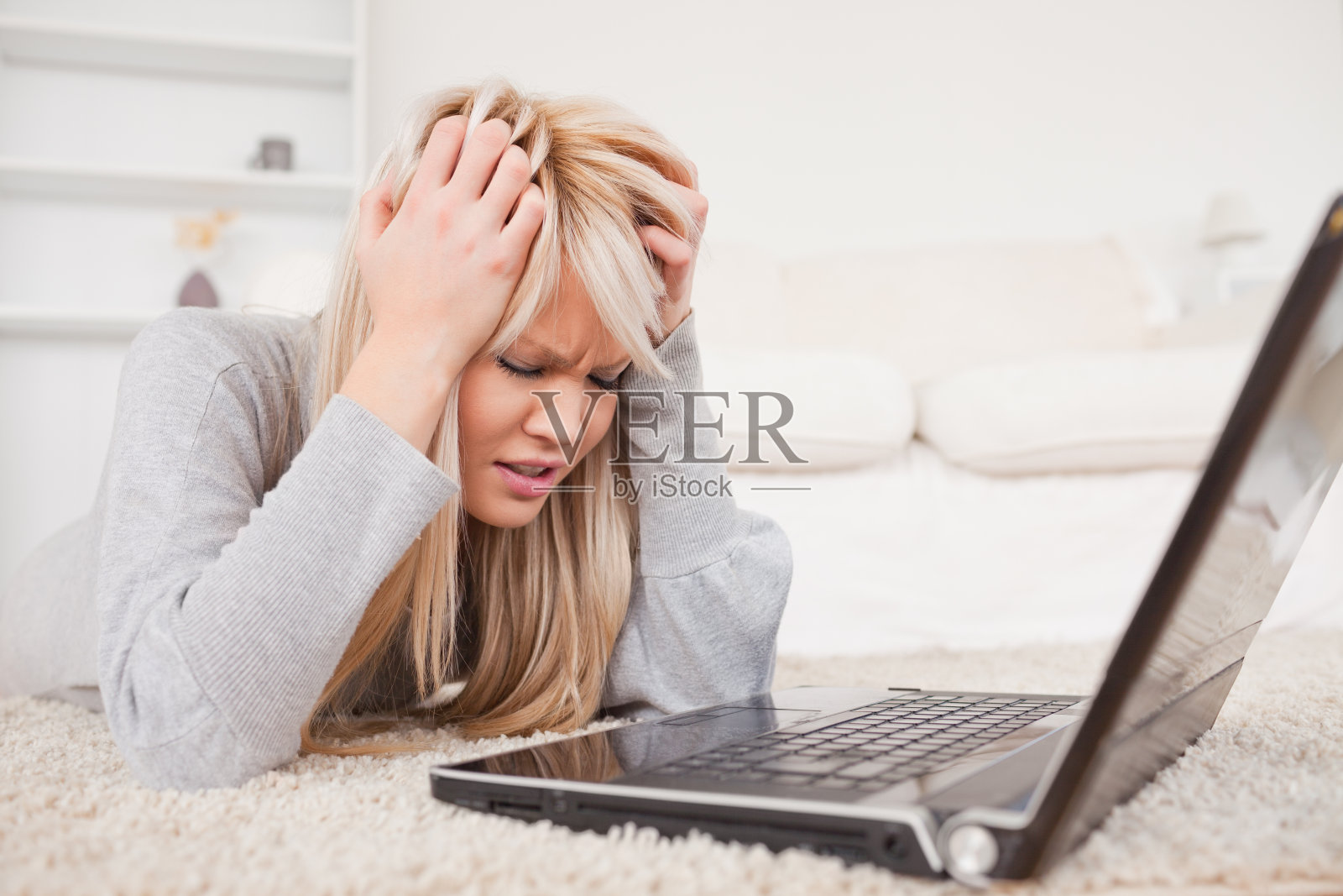 迷人的金发女人生气她的电脑躺在地毯上照片摄影图片