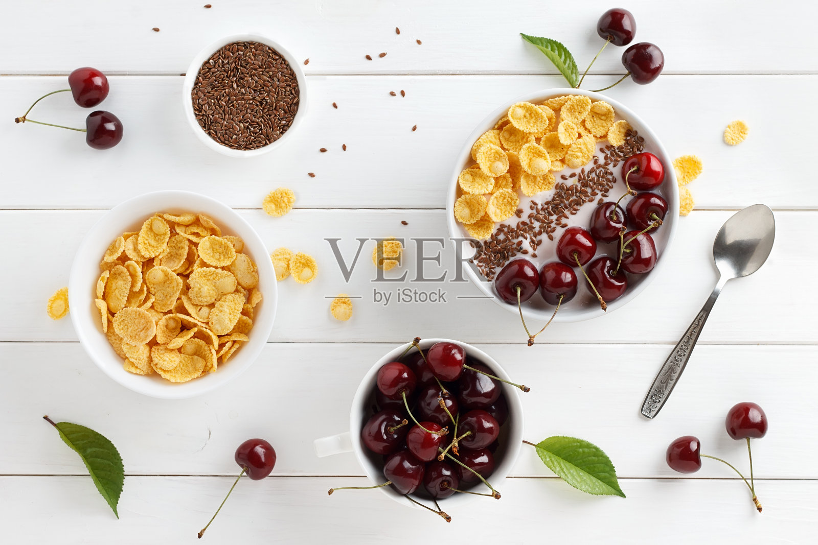 夏日健康早餐:白色木桌上的碗里有玉米片、希腊酸奶、甜樱桃和亚麻籽。照片摄影图片