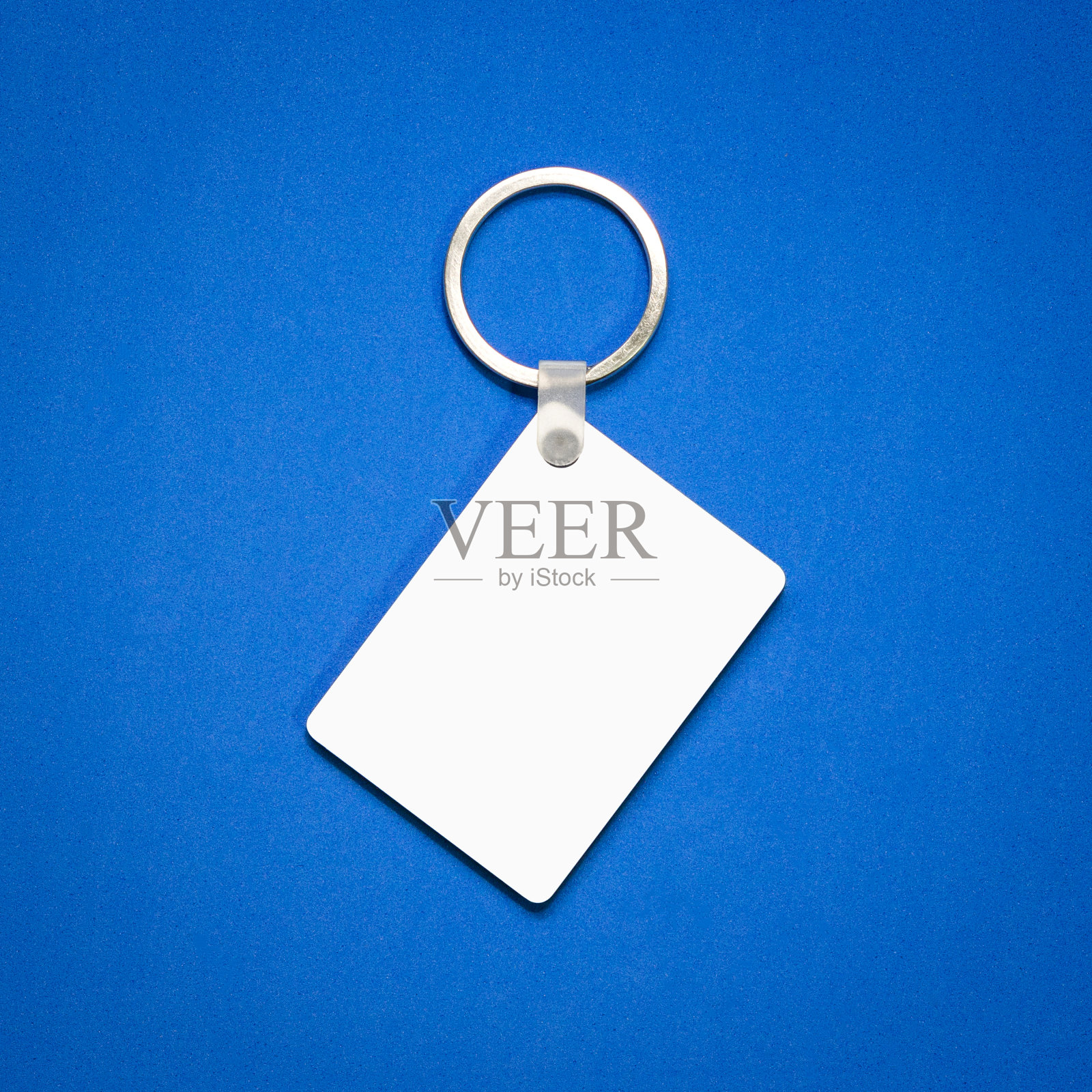 蓝色背景上的白色钥匙圈。为您设计的钥匙链。悬挂的装饰品或纪念品。(矩形)照片摄影图片