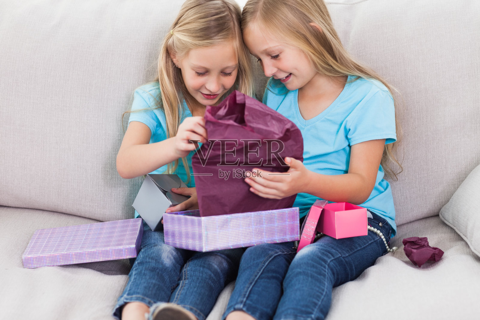 一对年轻的双胞胎坐在沙发上打开生日礼物照片摄影图片