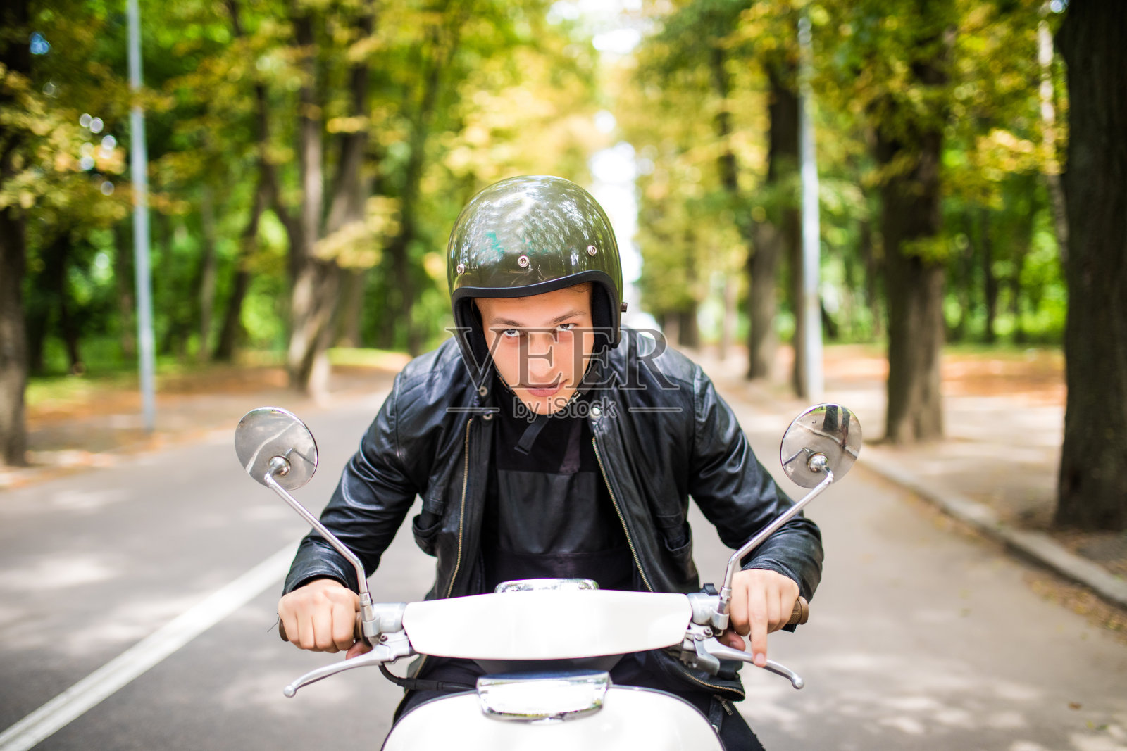 一个戴着头盔的兴高采烈的年轻人正在城里骑摩托车。照片摄影图片