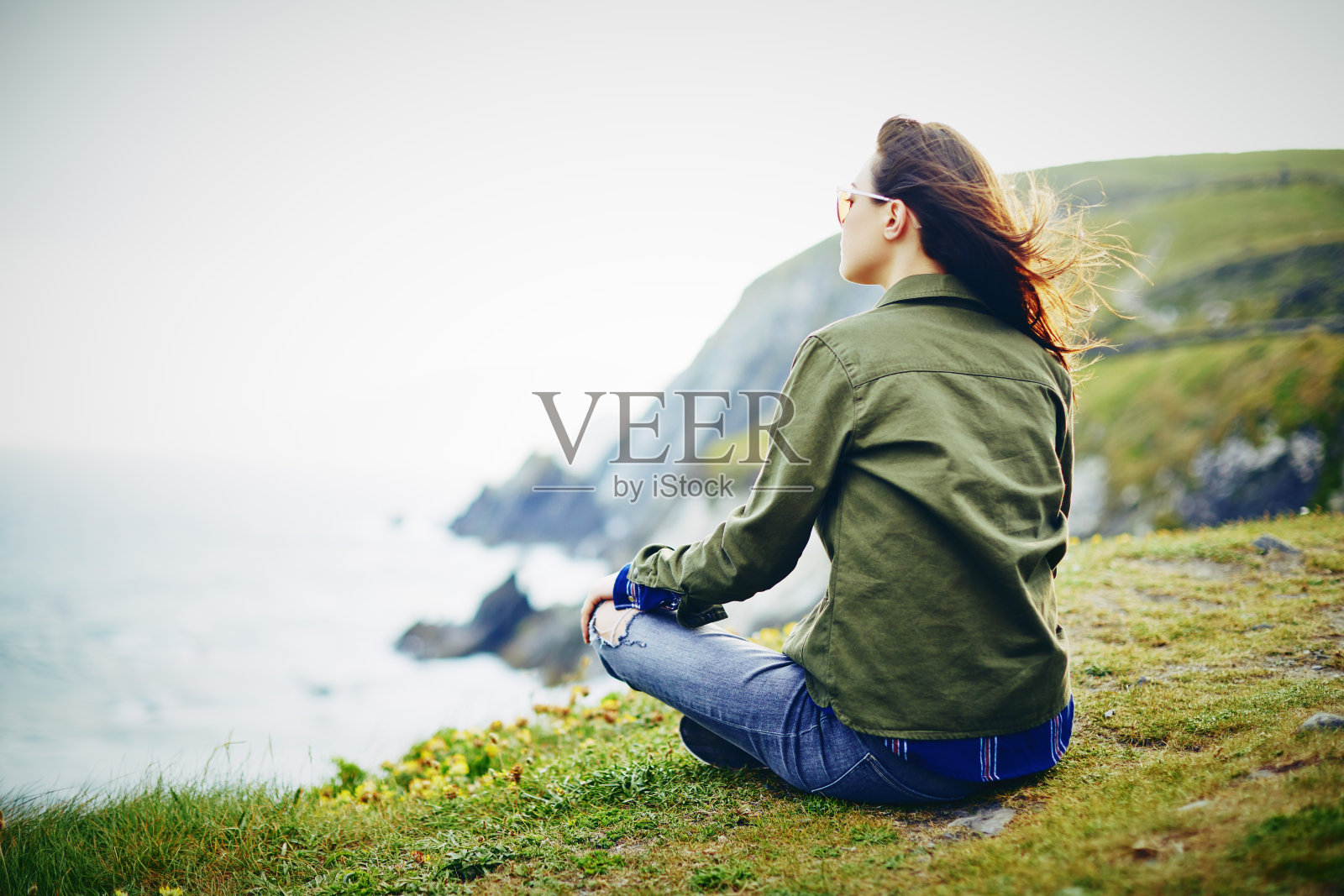 坐在长满草的悬崖上看海景的女人照片摄影图片