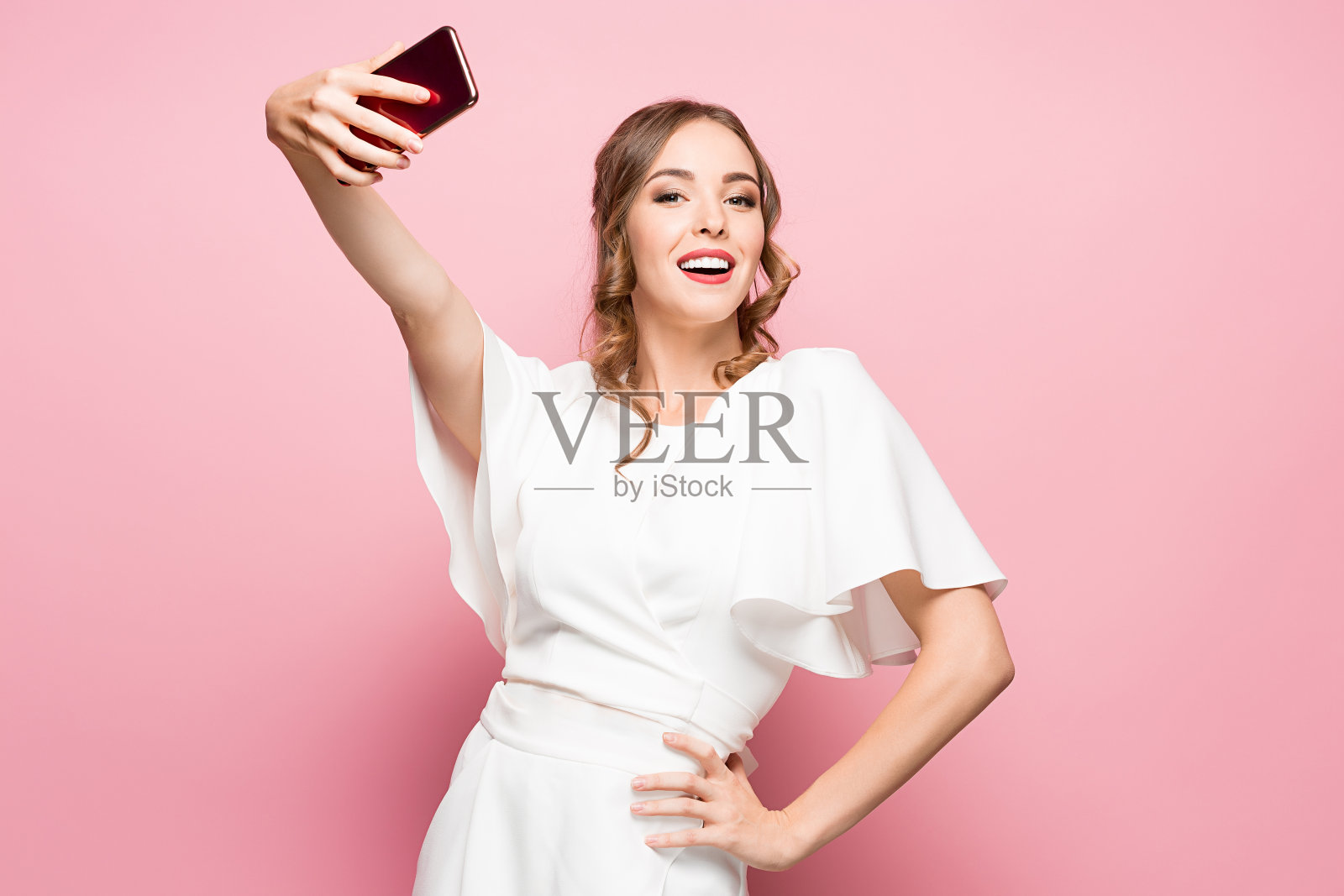 一个年轻迷人的女人用粉色背景的智能手机自拍的肖像照片摄影图片