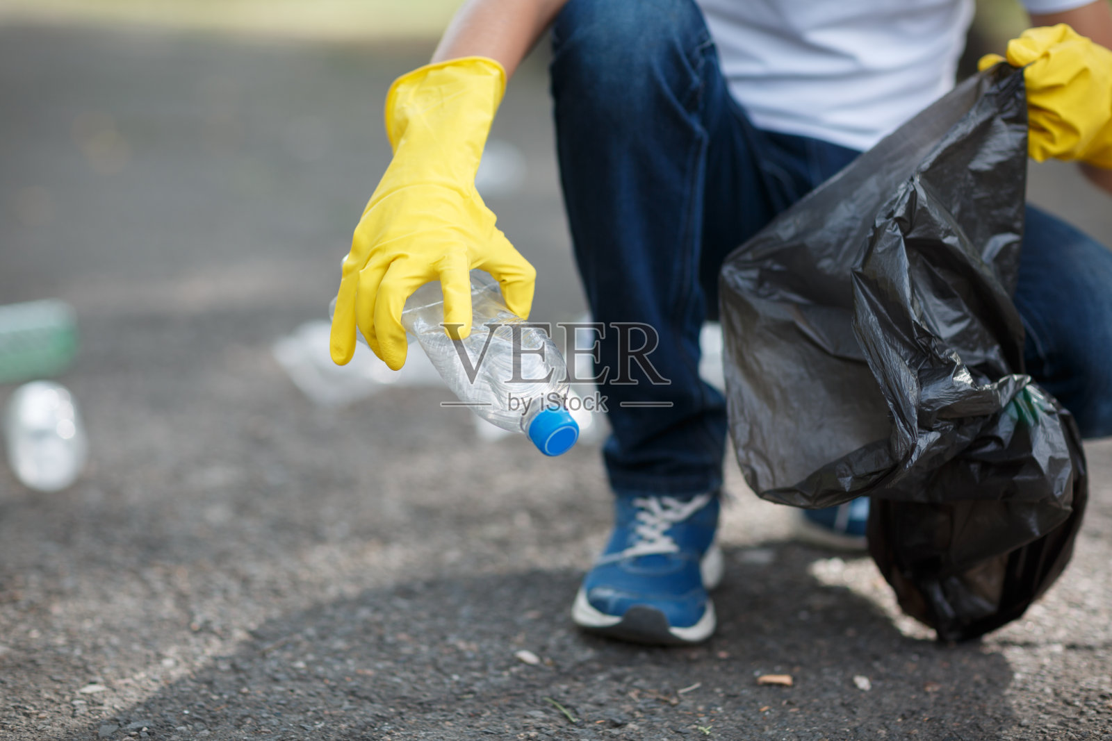男子双手戴着黄色橡胶手套，将生活垃圾放入外面的黑色小垃圾袋里。照片摄影图片