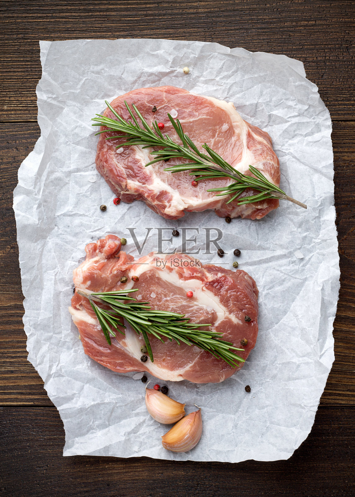 新鲜的猪肉排放在白色羊皮纸上，以迷迭香，大蒜和香料为背景。照片摄影图片