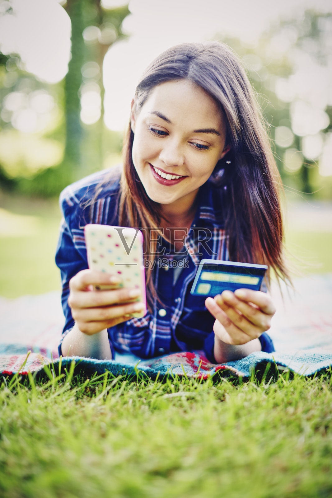 微笑的年轻女子拿着智能手机和信用卡在公园里照片摄影图片