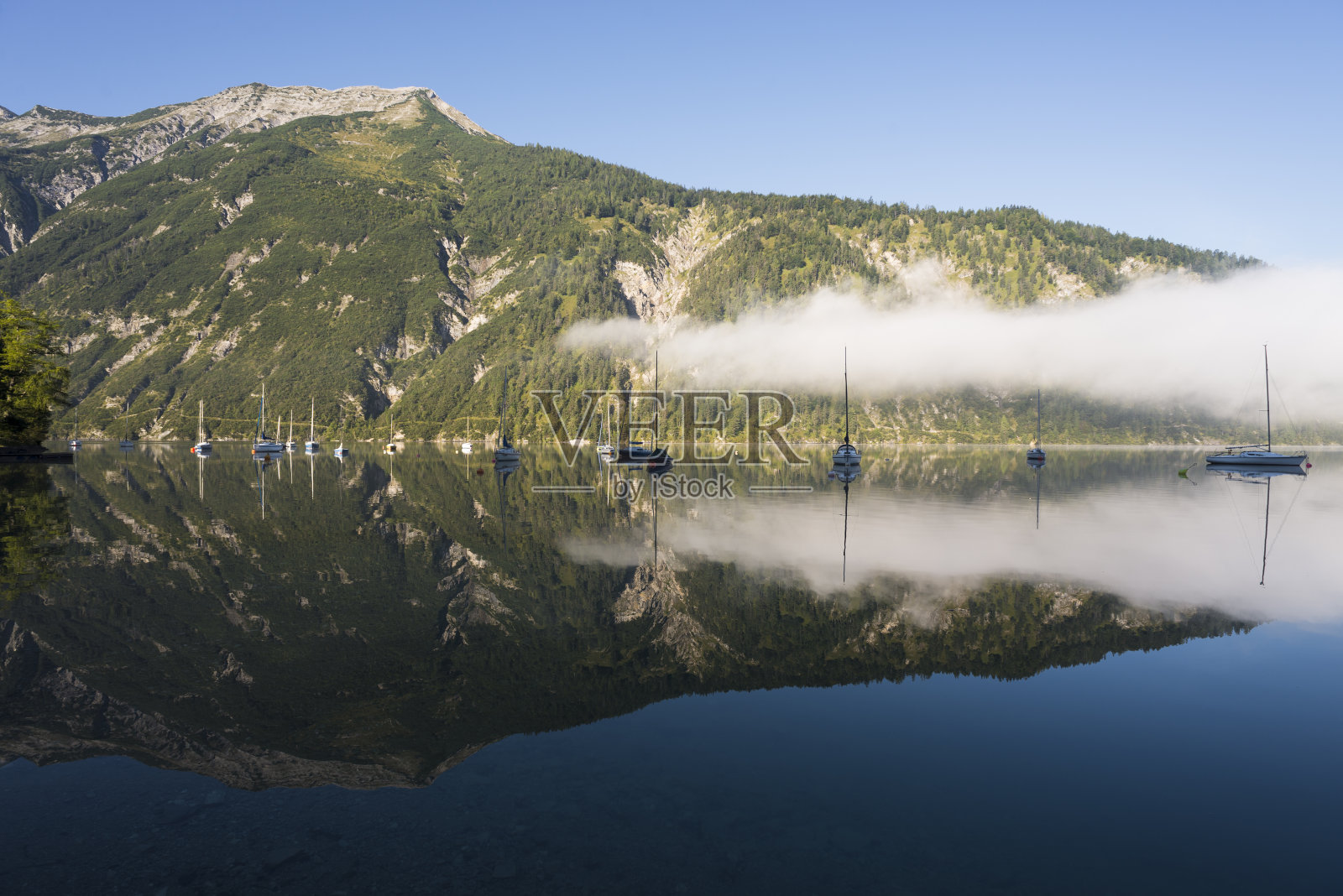 奥地利蒂罗尔的秋天，晨曦中的薄雾、群山、帆船和游艇倒映在阿琴湖平静的湖面上照片摄影图片