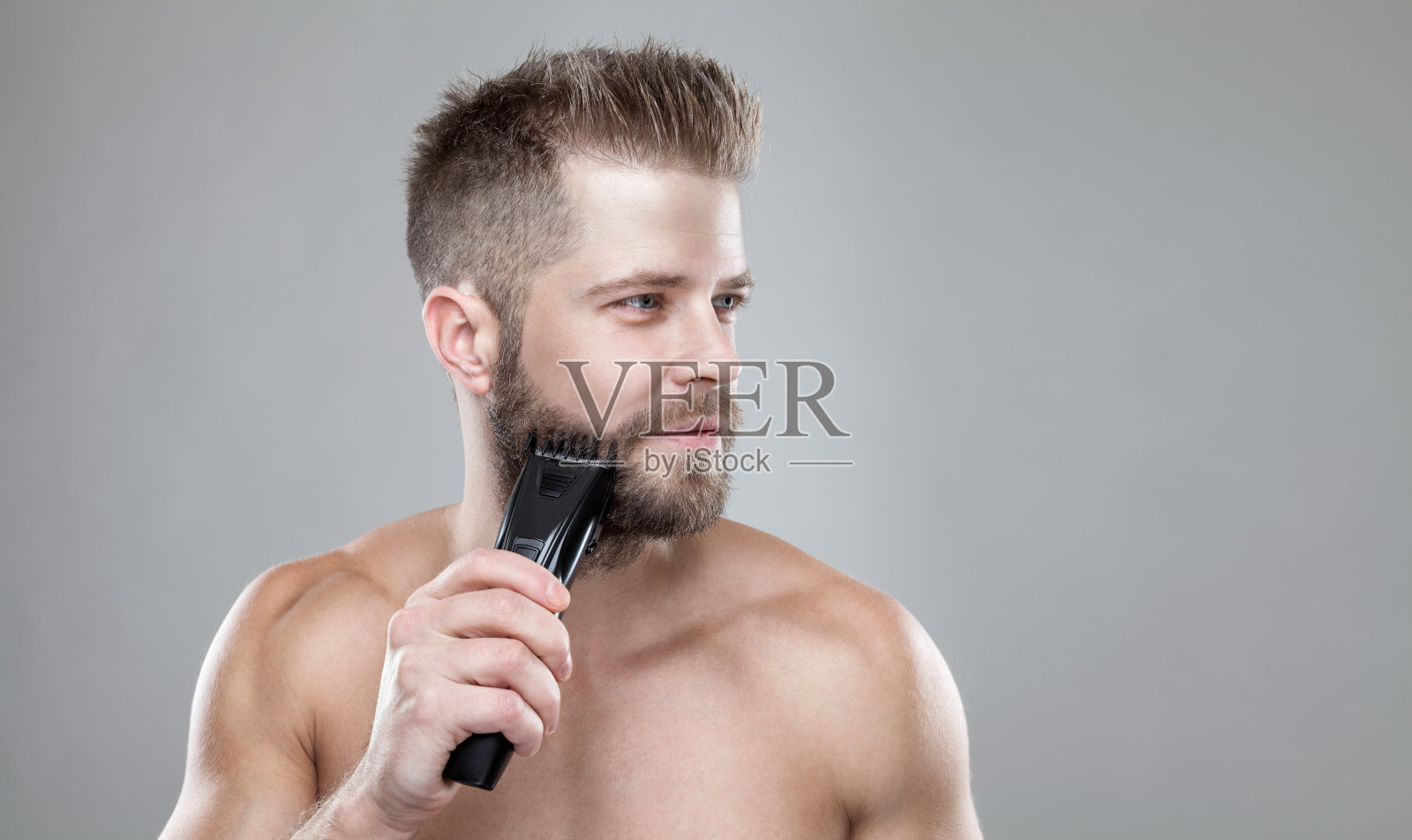英俊的蓄胡须的男人正在用修胡子机修胡子照片摄影图片