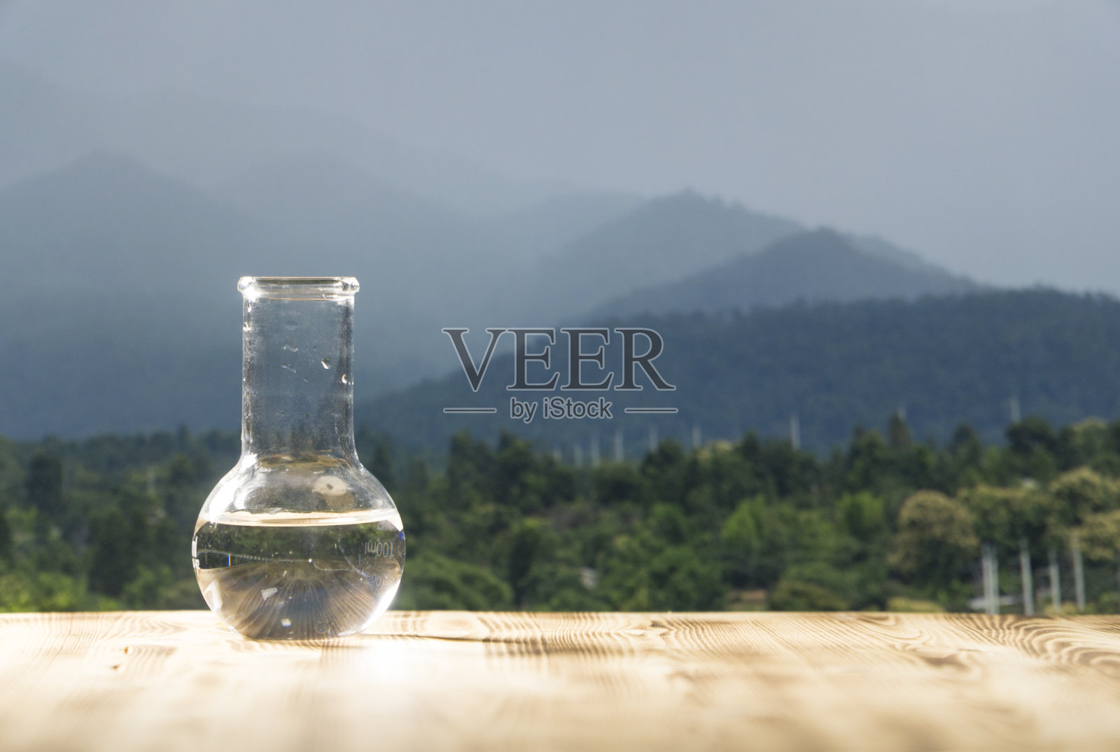 在山背景的木桌上的实验室玻璃烧瓶里装着干净的水。生态理念，水的纯净与品质的检验照片摄影图片