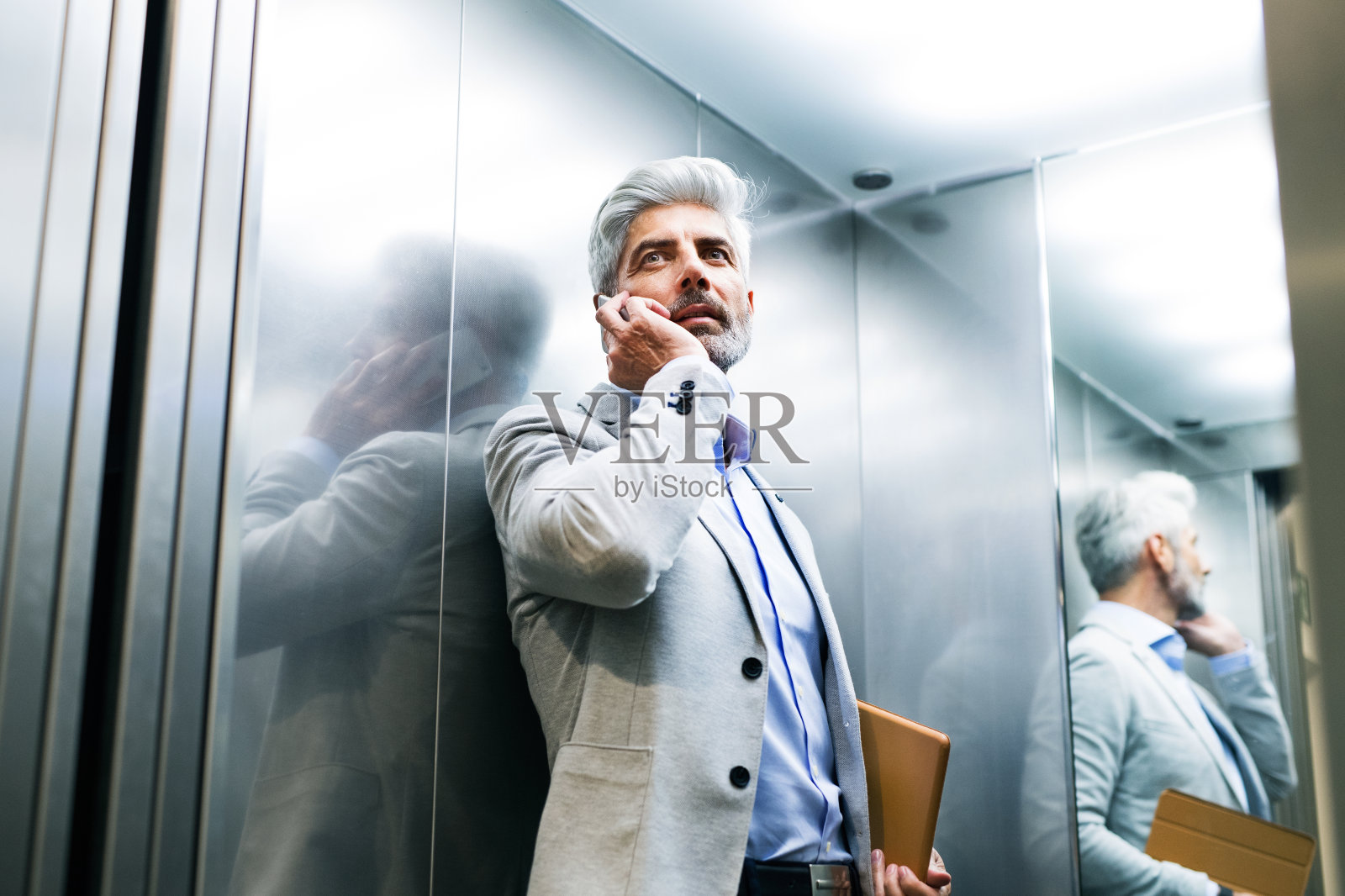 成熟的商人在电梯里用智能手机。照片摄影图片