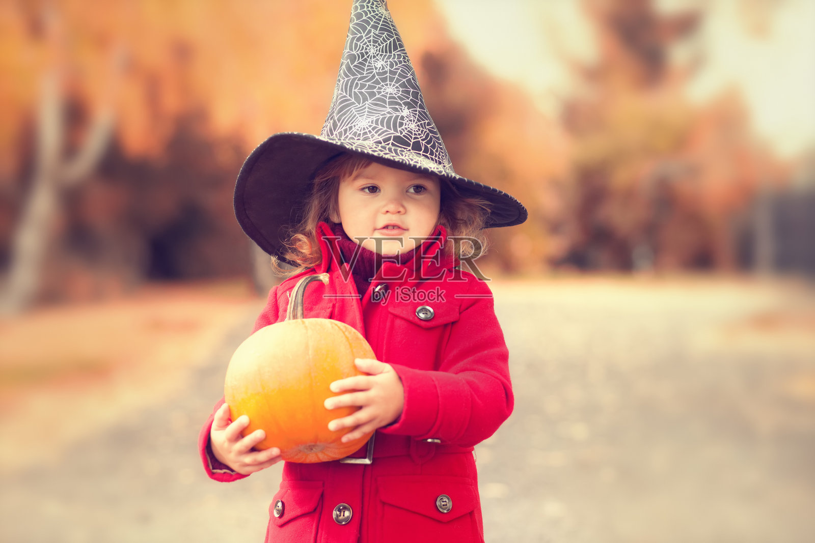 小女孩戴着万圣节的女巫帽，穿着暖和的红色外套，在秋天的日子里玩得很开心。照片摄影图片
