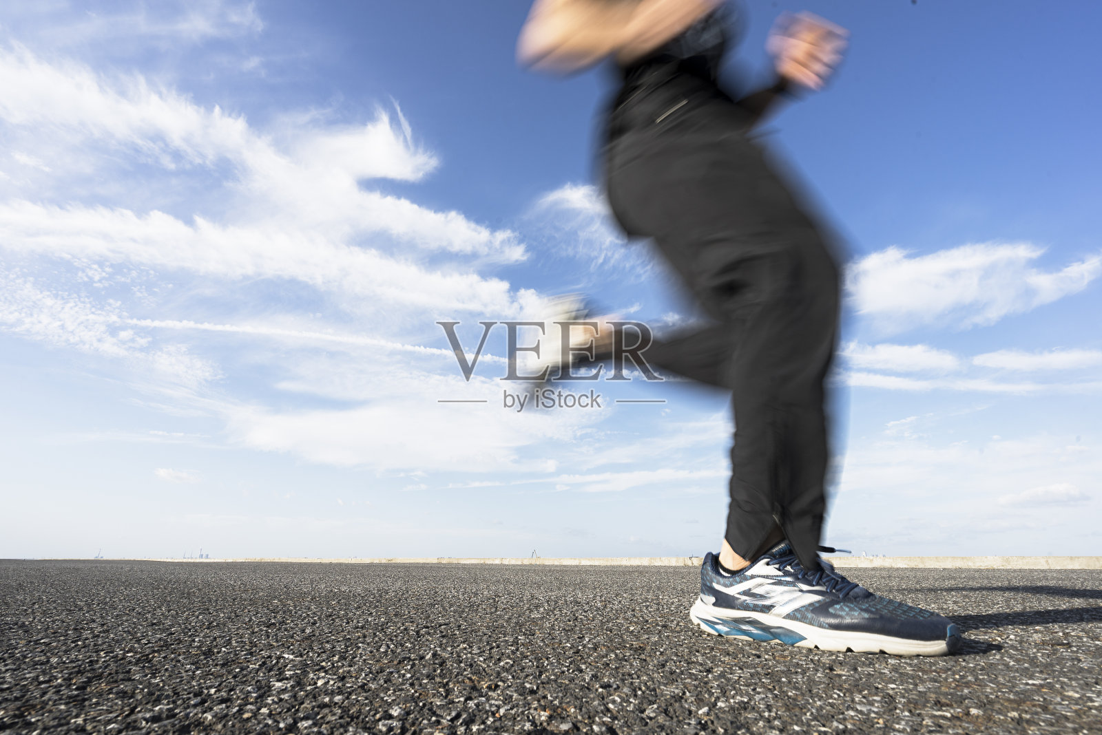 年轻的男运动员在柏油路上迎着天空奔跑照片摄影图片