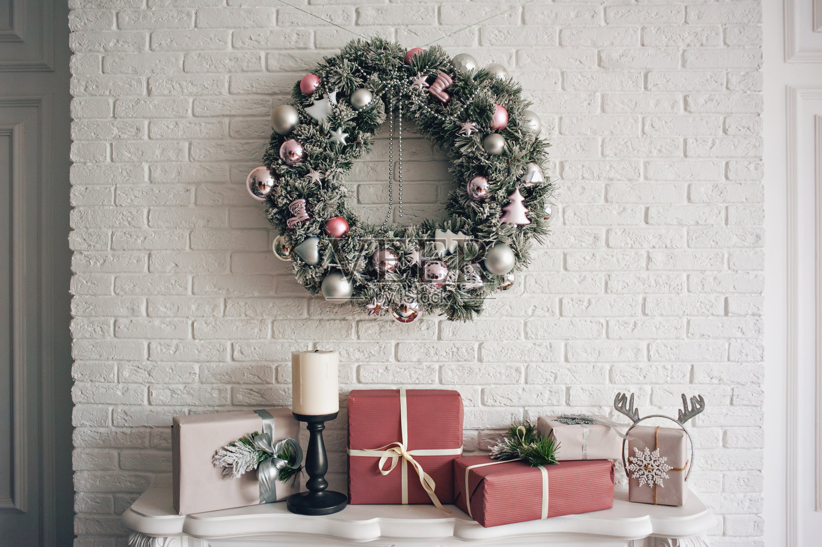 一个传统的明亮的圣诞花环挂在壁炉上方的白色砖墙上，包装好的礼物和蜡烛堆放在壁炉上。照片摄影图片