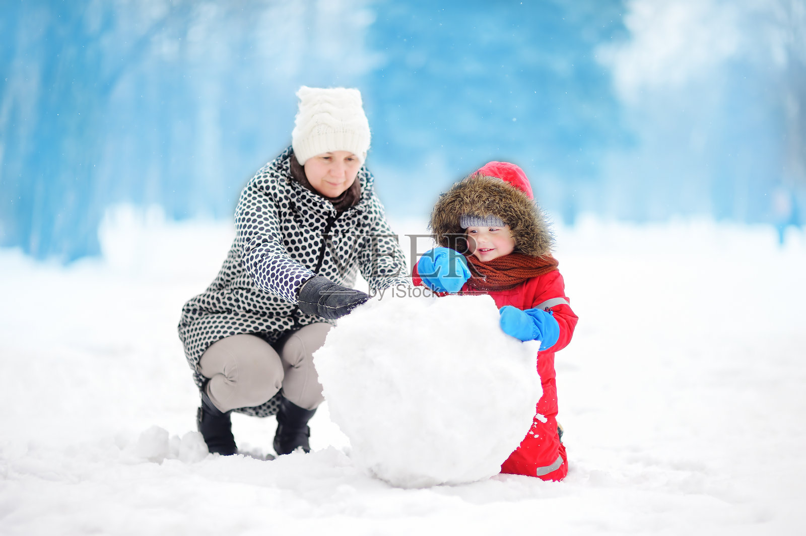 小男孩和他的妈妈/保姆/奶奶在下雪的公园堆雪人照片摄影图片