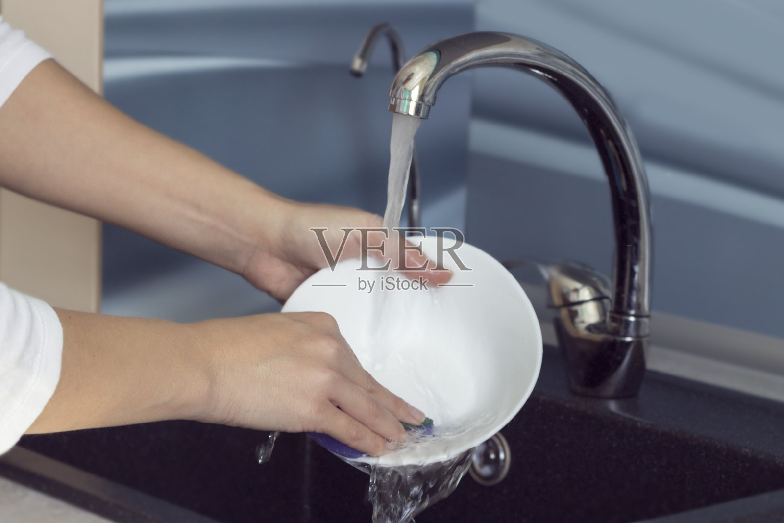 女人用手在水槽里的流水下洗盘子。照片摄影图片