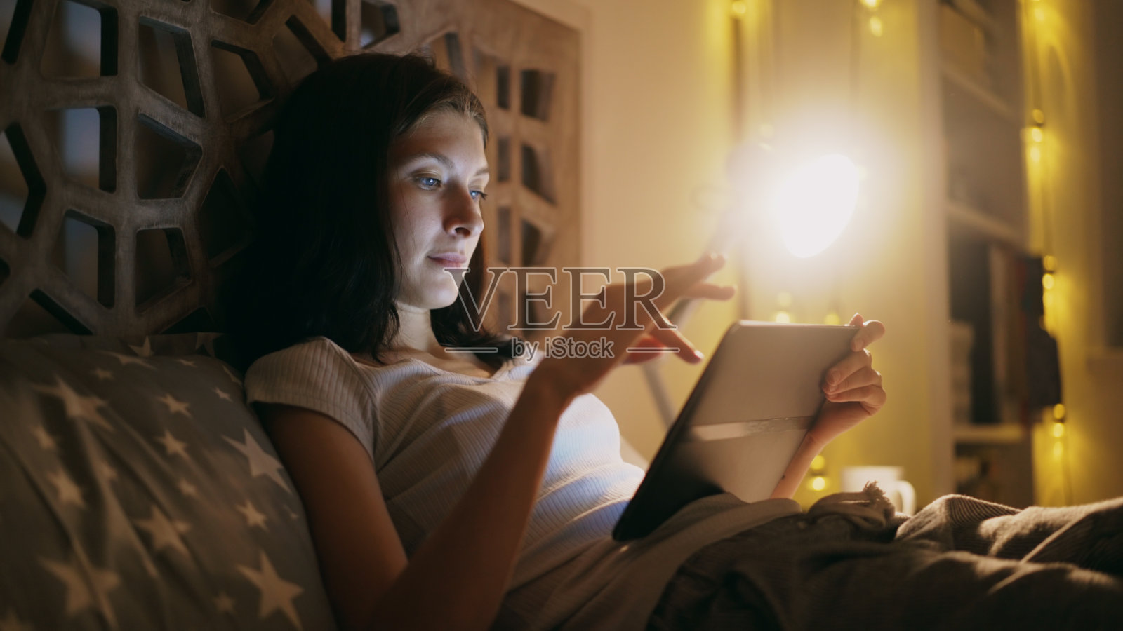 一个年轻专注的女人晚上躺在家里的床上用平板电脑看网络新闻的特写照片摄影图片