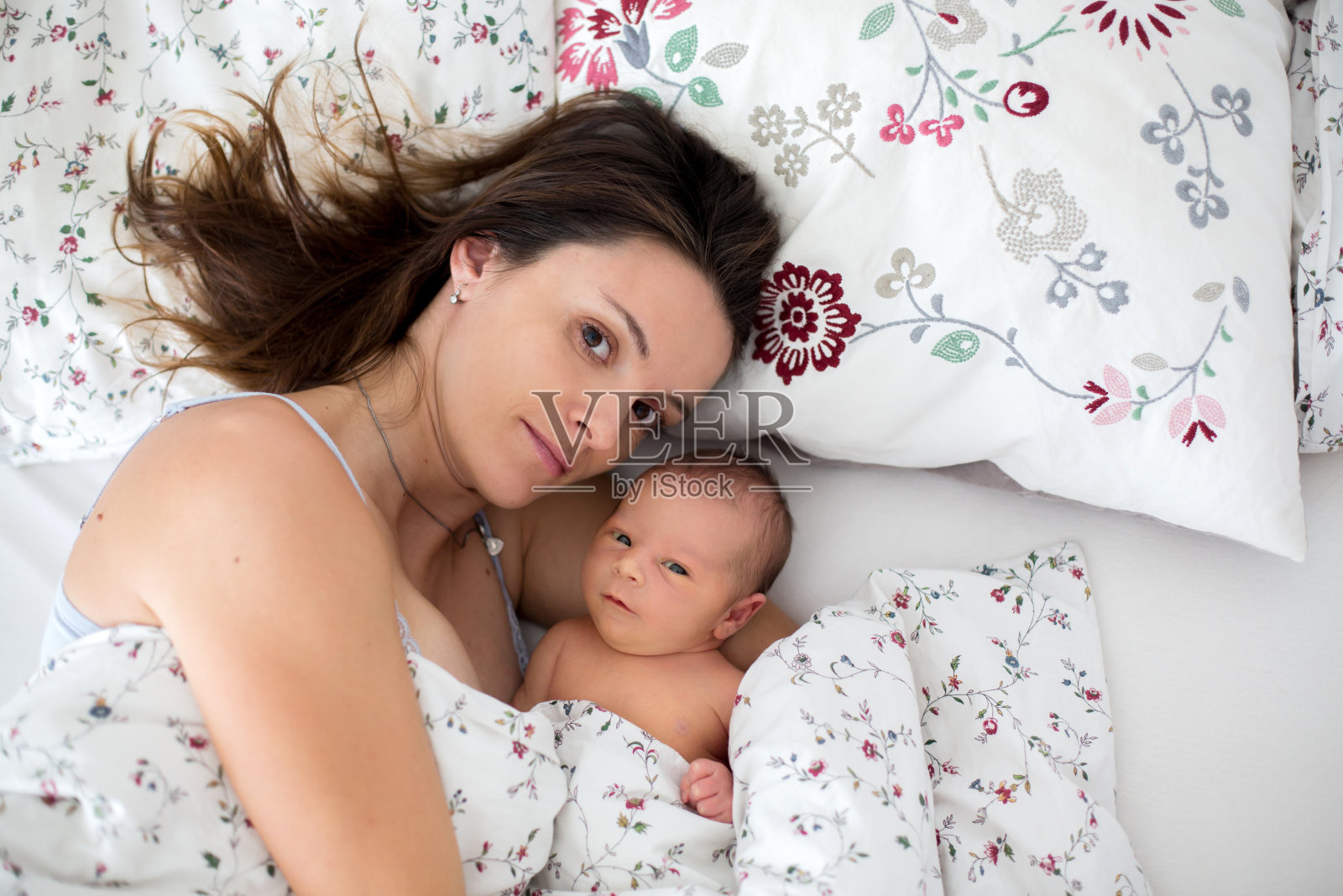 年轻的母亲和她刚出生的男婴躺在床上照片摄影图片