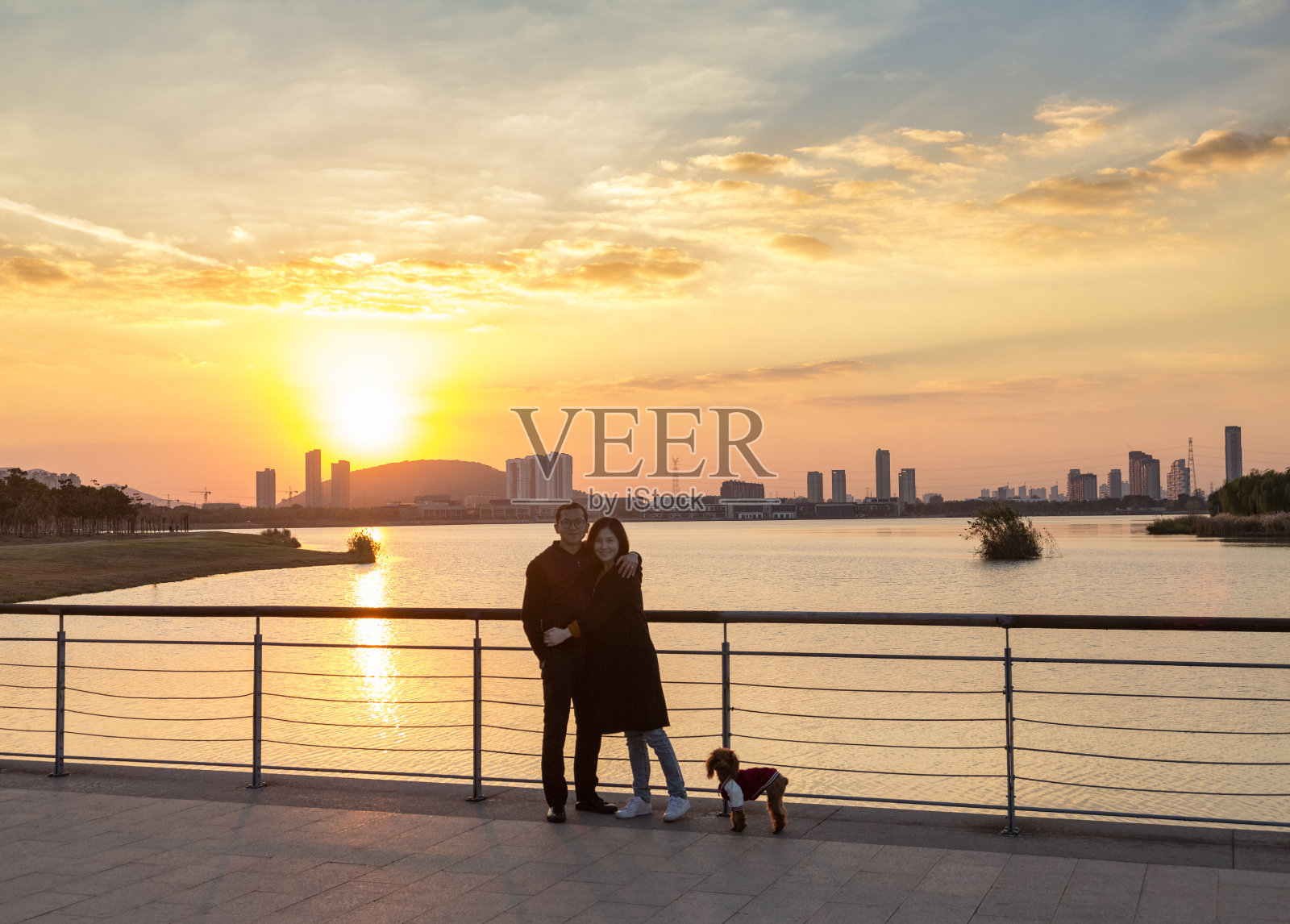 年轻夫妇和他们的小狗对着日落的天空摆姿势照片摄影图片
