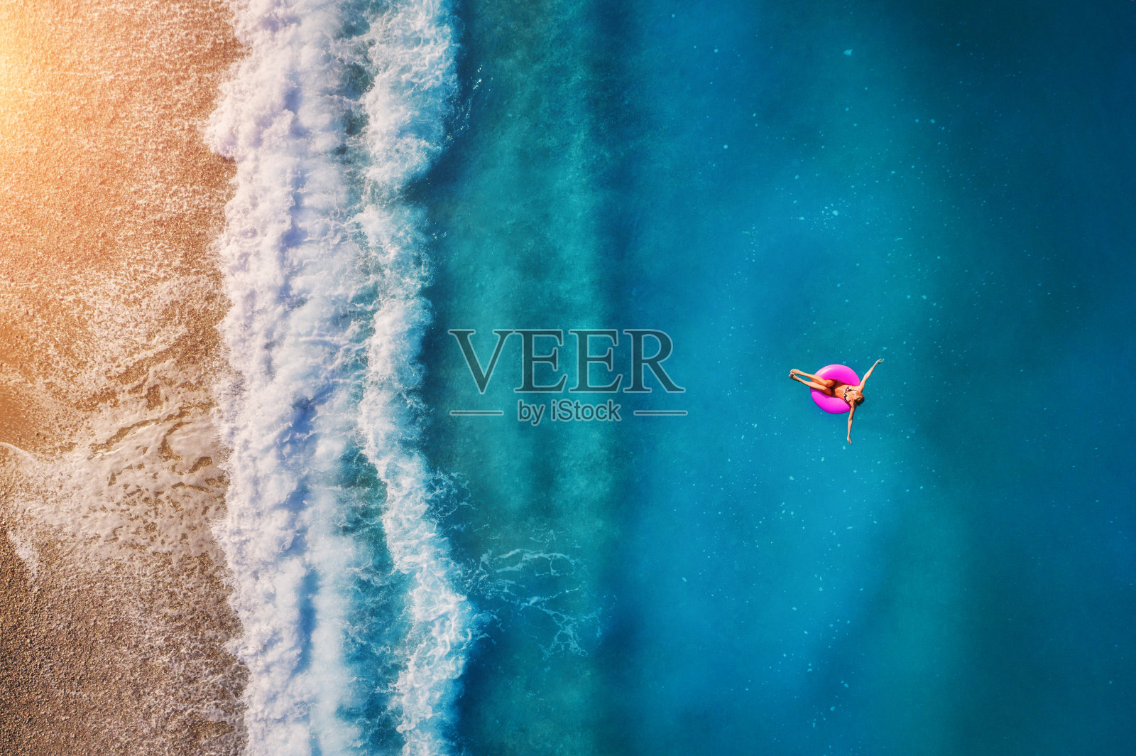 鸟瞰图上的年轻女子游泳在粉红色的游泳环在透明的绿松石海在Oludeniz。夏天的海景，沙滩，美丽的海浪，蓝色的水在日落。无人机俯视图照片摄影图片