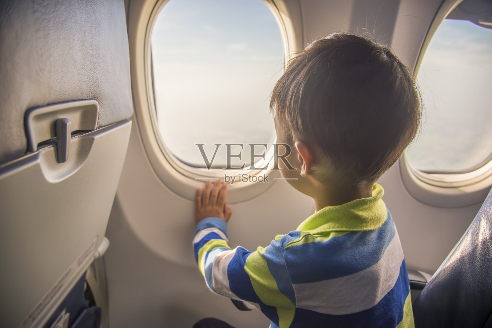 亚洲男孩坐在飞机座位上看飞机窗外的天空和云的鸟瞰图。照片摄影图片