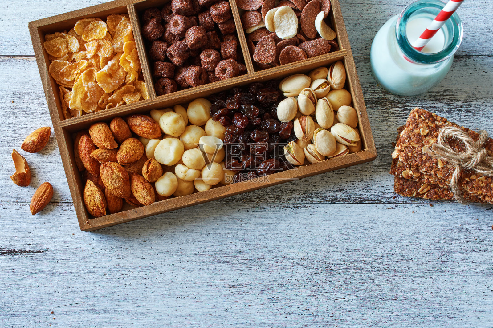 俯视图各种坚果，谷物和葡萄干在木制的盒子，自制的燕麦条和杏仁牛奶在白色的桌子。照片摄影图片