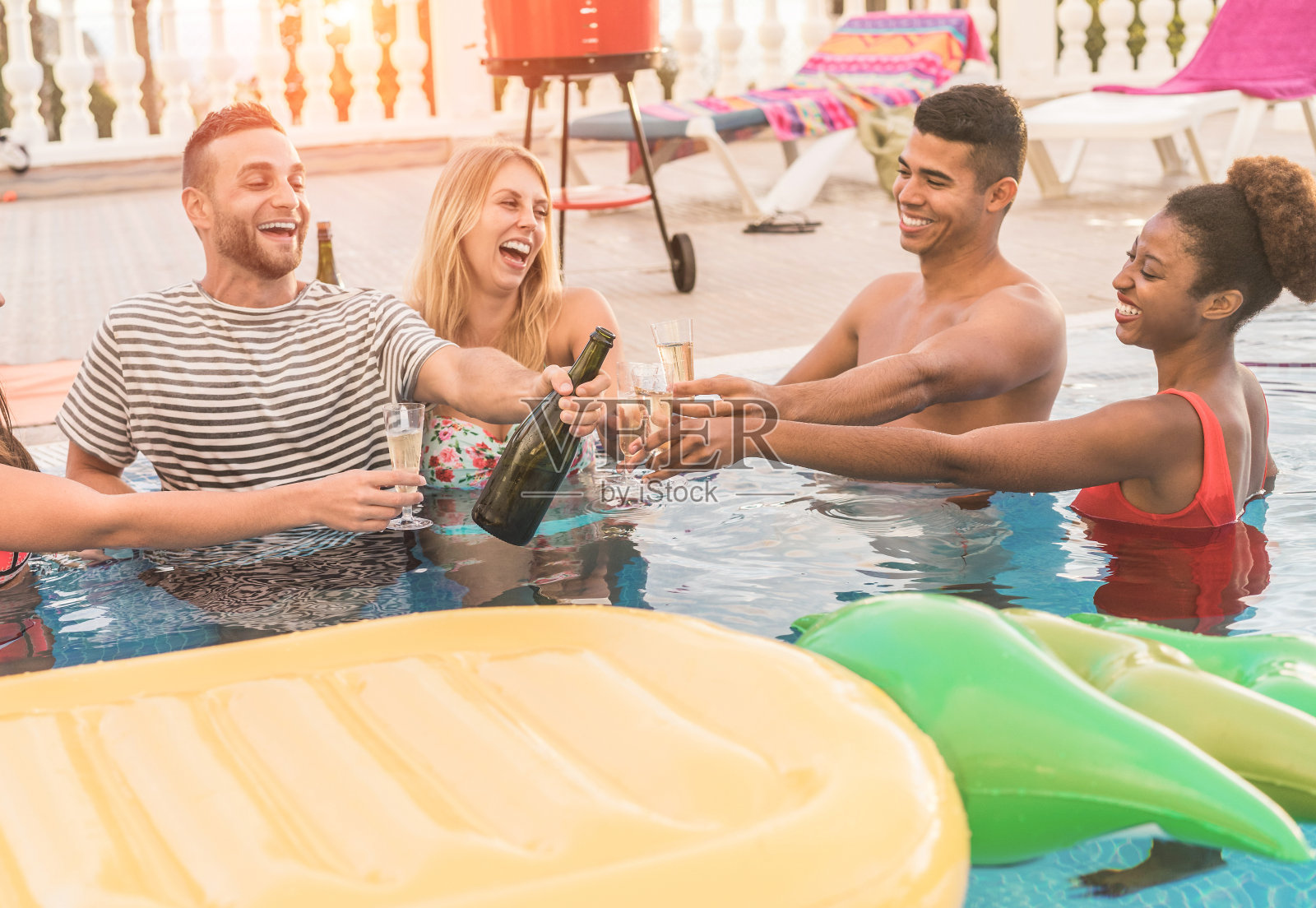 快乐的朋友在夕阳下的泳池派对上用香槟欢呼-富人们在专属的热带户外度假-假日，青年生活方式和友谊概念-专注于眼镜照片摄影图片