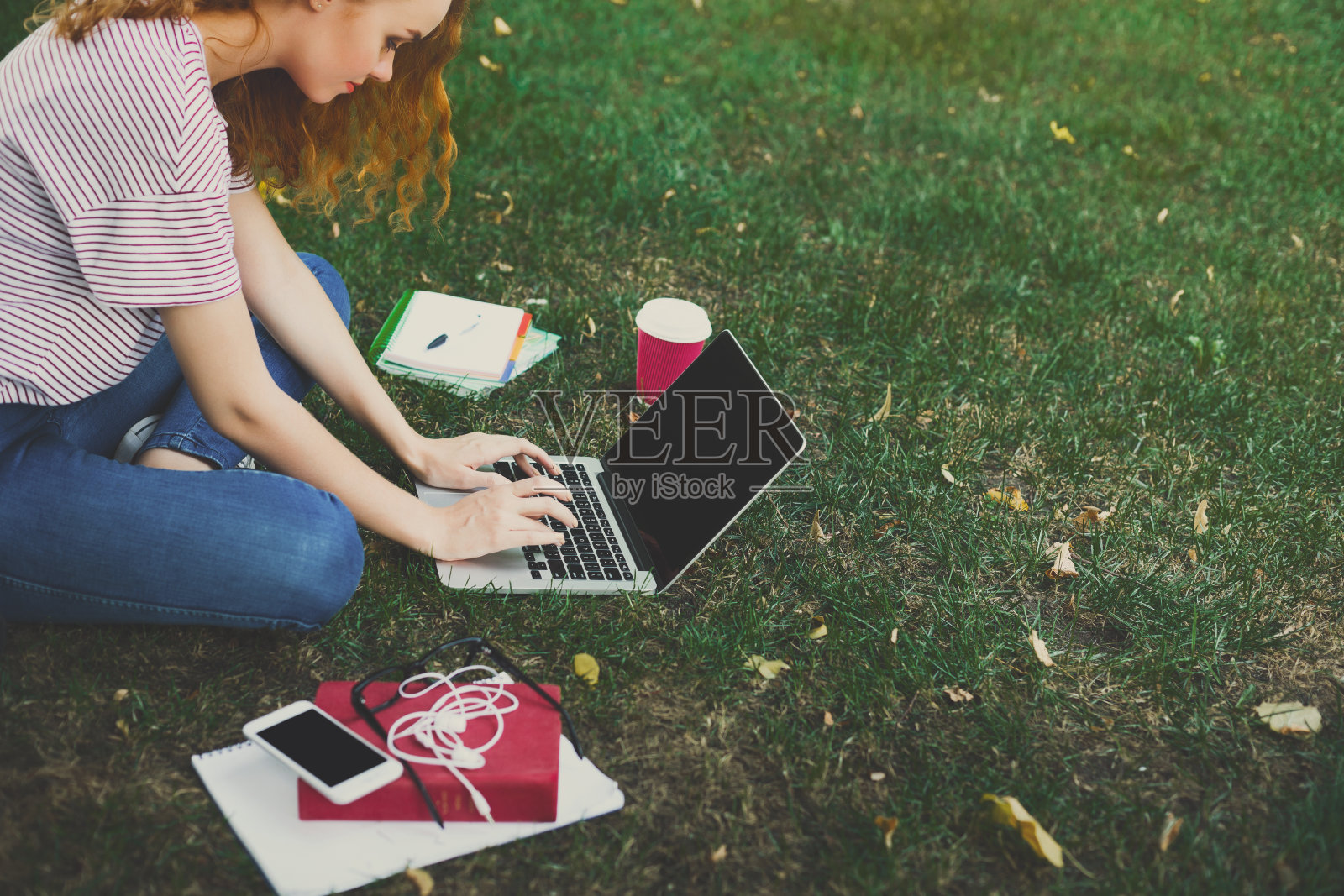 年轻的红发女孩坐在树下随意使用笔记本电脑照片摄影图片