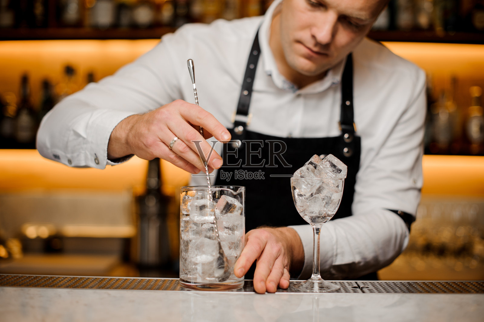 年轻的酒吧招待正在搅拌玻璃杯里的冰块照片摄影图片