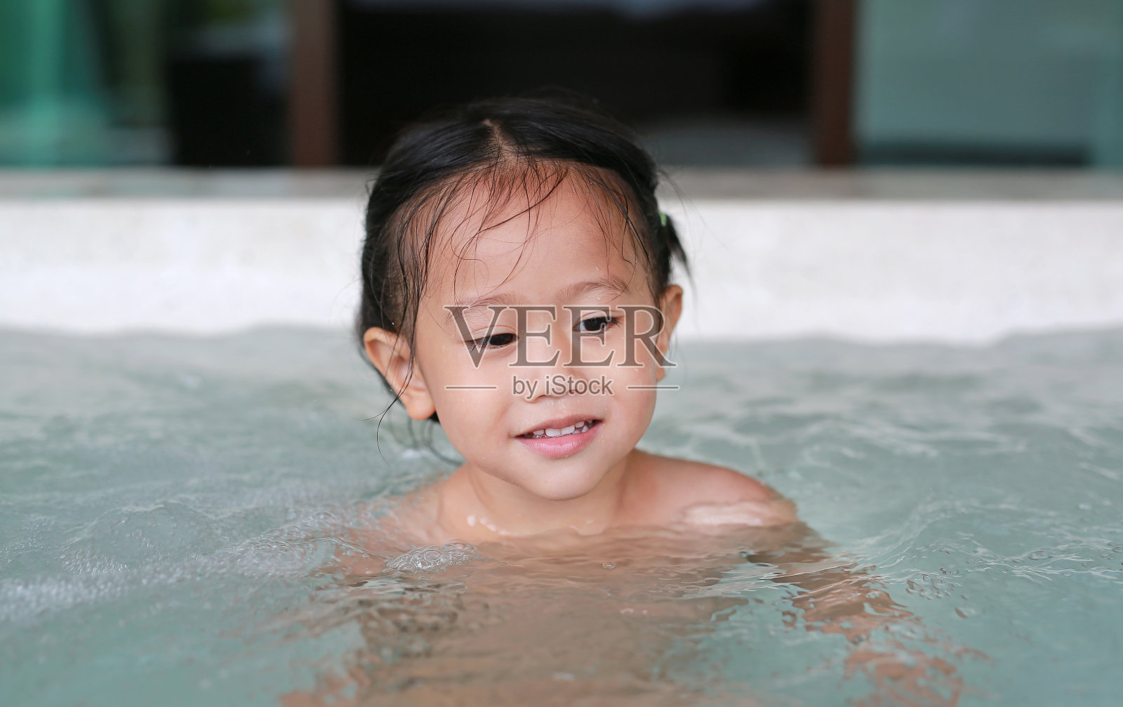 快乐的亚洲小女孩躺在热水浴缸里。照片摄影图片