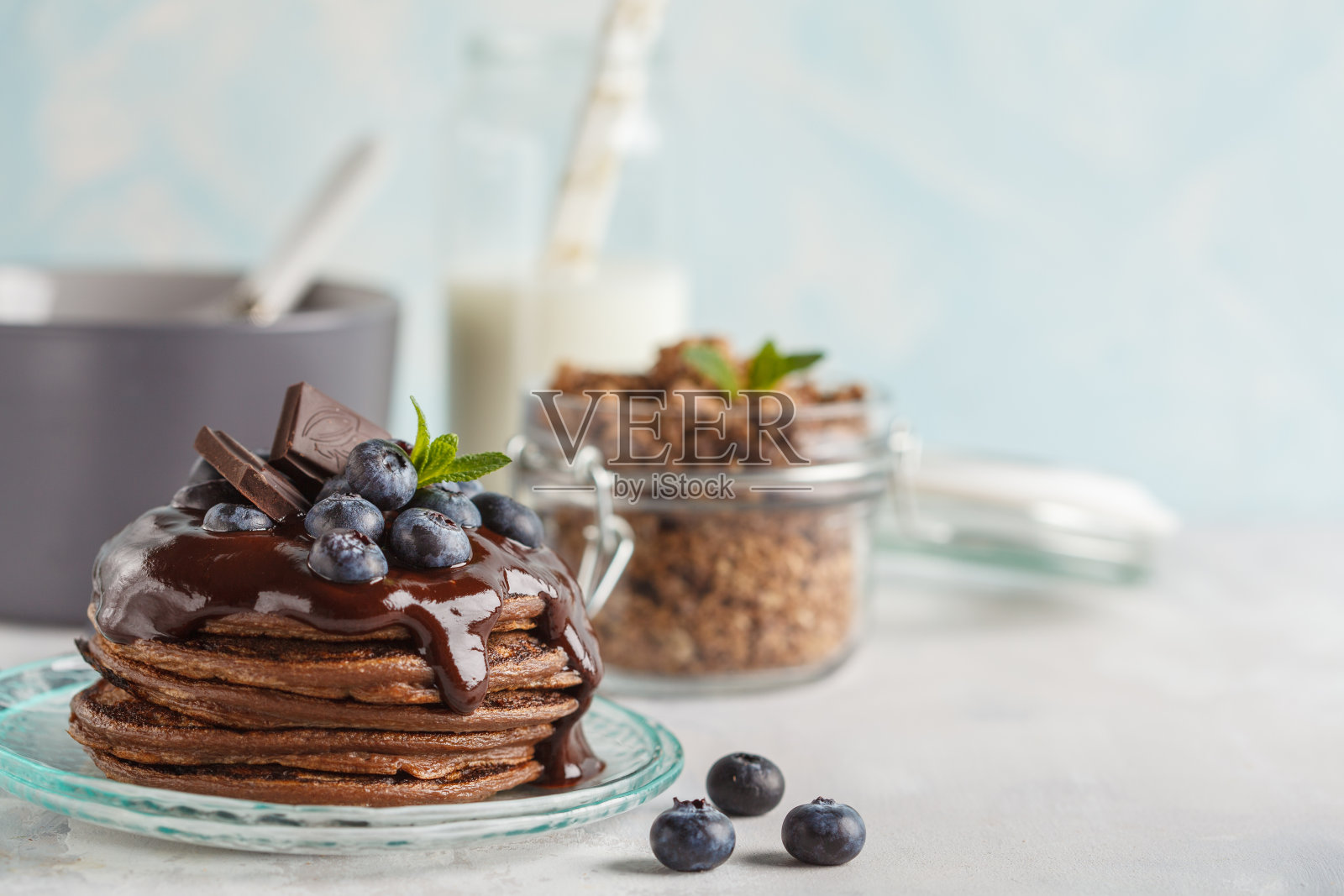 巧克力煎饼加糖浆和浆果，巧克力格兰诺拉麦片和牛奶。早餐概念，蓝色背景，拷贝空间照片摄影图片