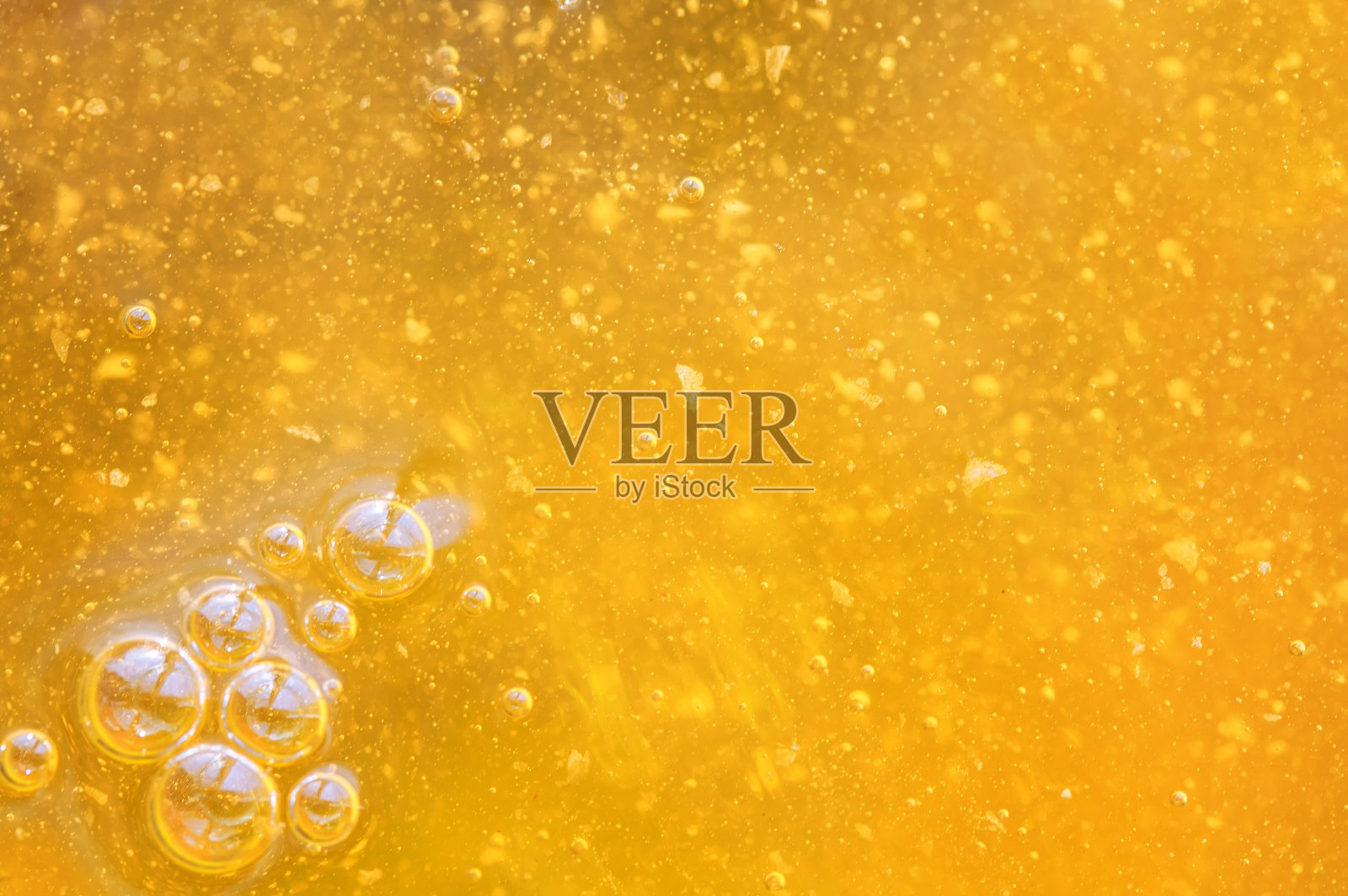 美味的液体背景新鲜的金色蜂蜜，泡沫在阳光下闪闪发光。照片摄影图片