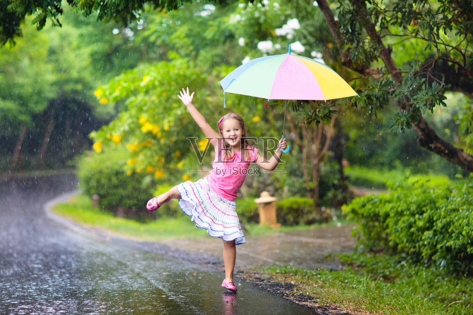 孩子们撑着伞在夏日的雨中玩耍。照片摄影图片