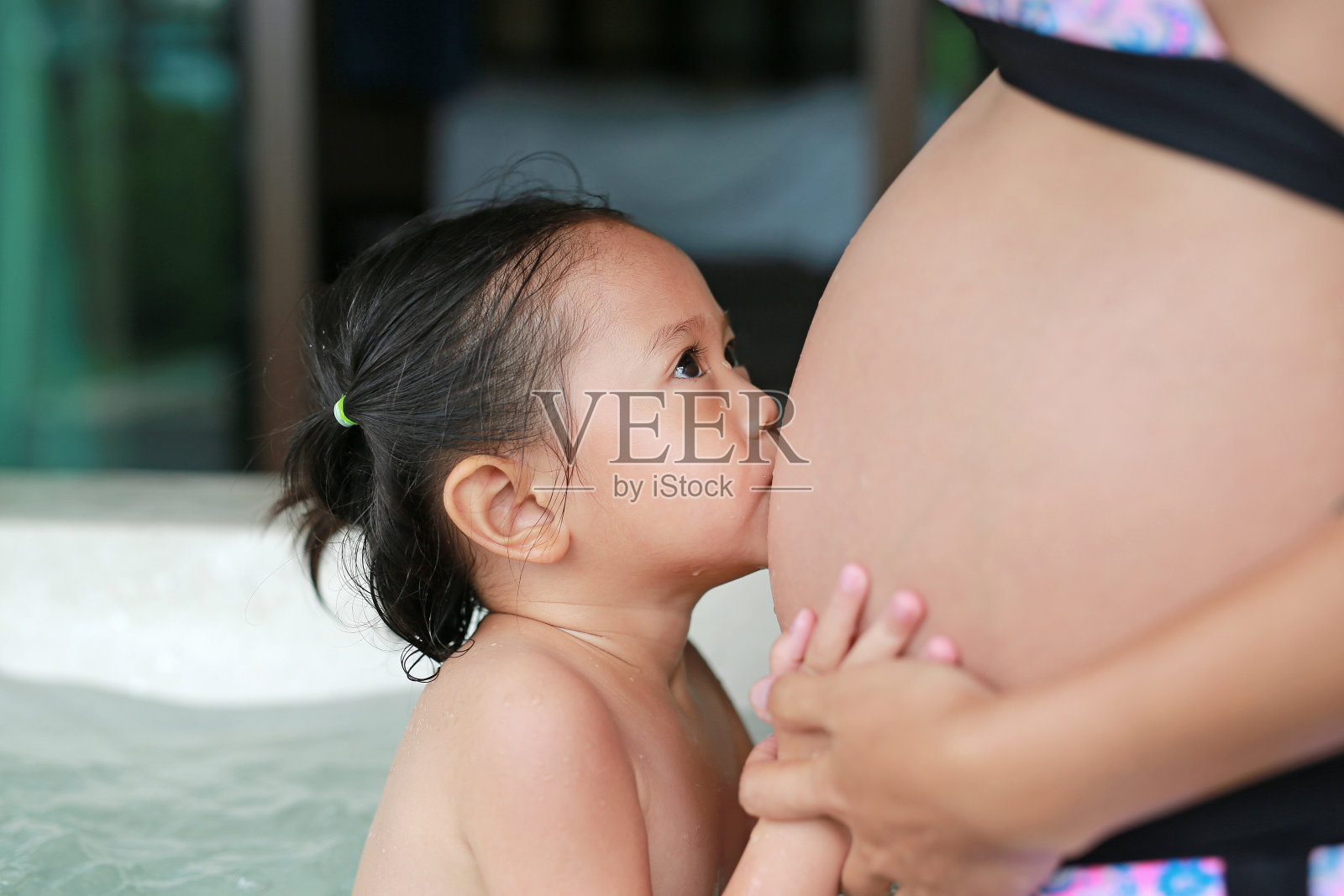 亚洲小女孩在浴缸里亲吻孕妇的肚子。照片摄影图片