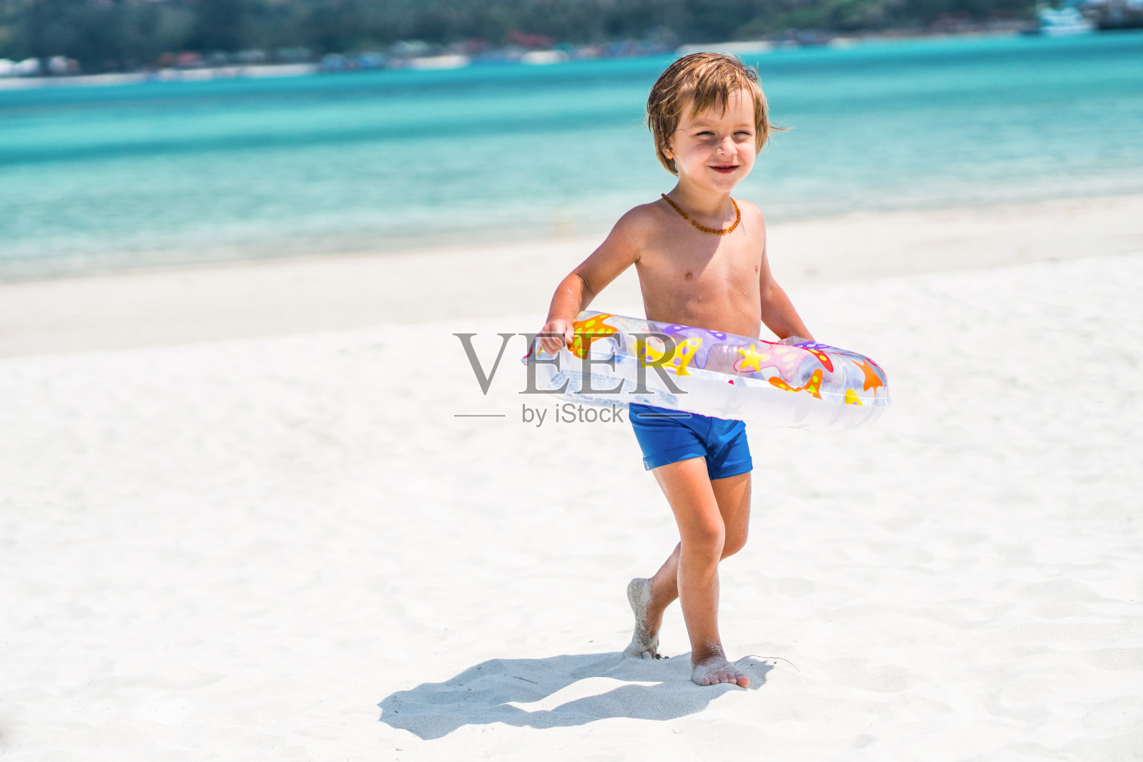 微笑的小男孩走在海滩上充气的戒指。照片摄影图片