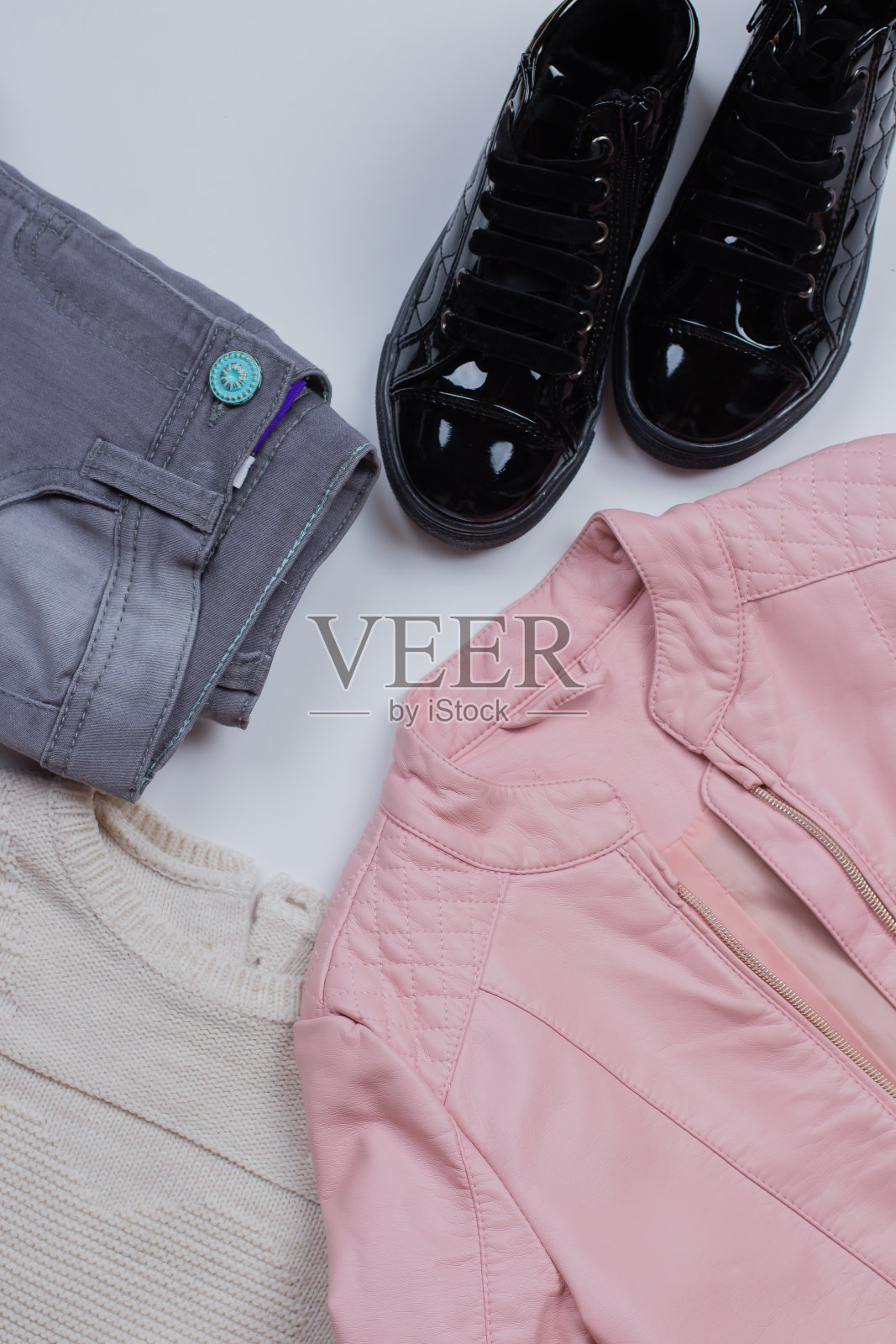 女人时尚服装。灰色牛仔裤，针织毛衣，粉粉色皮夹克，漆皮鞋靴子在白色背景，平lay，顶视图。照片摄影图片